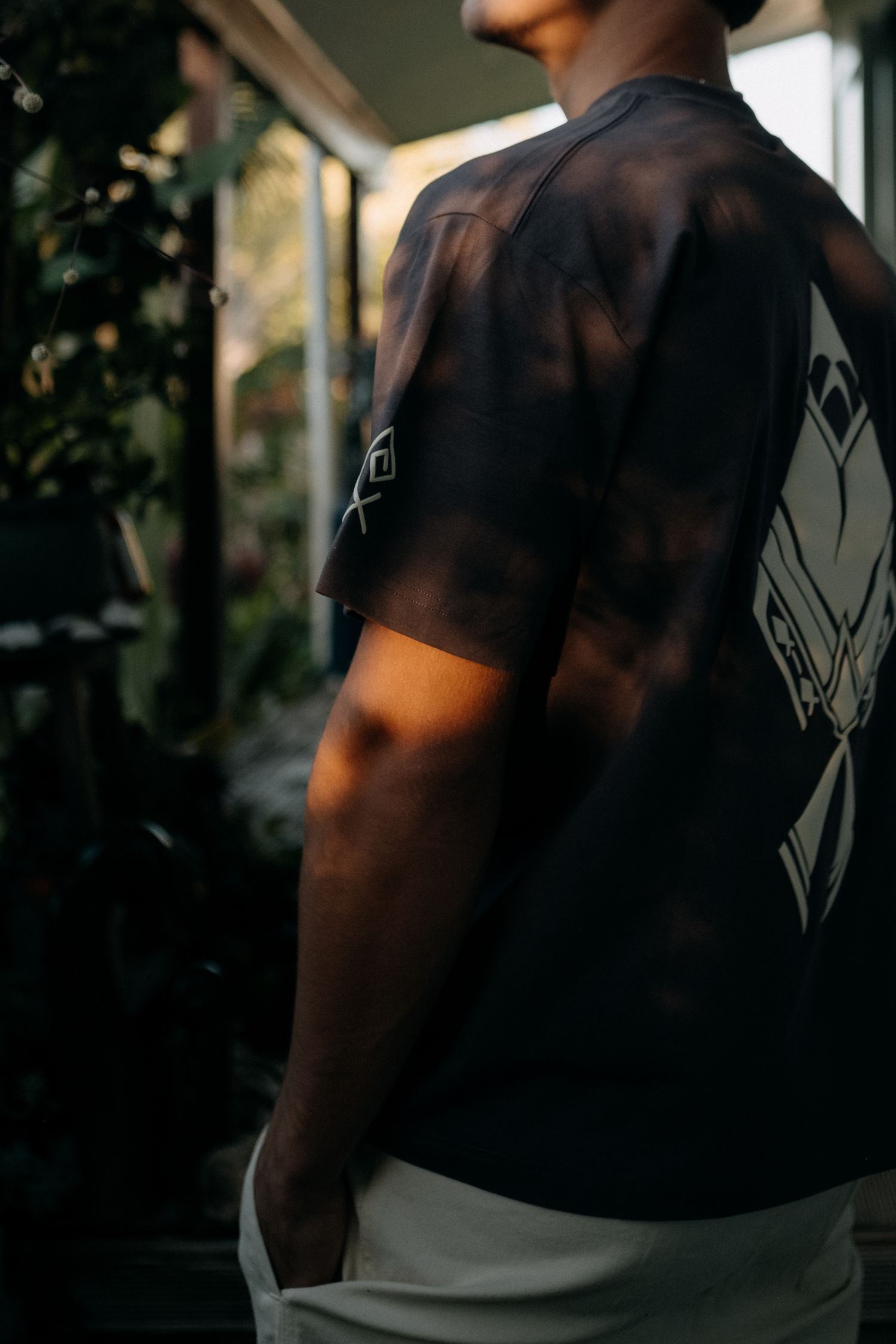 Person wearing a dark tie-dye graphic t-shirt with white printed design, standing in a sunlit indoor space.