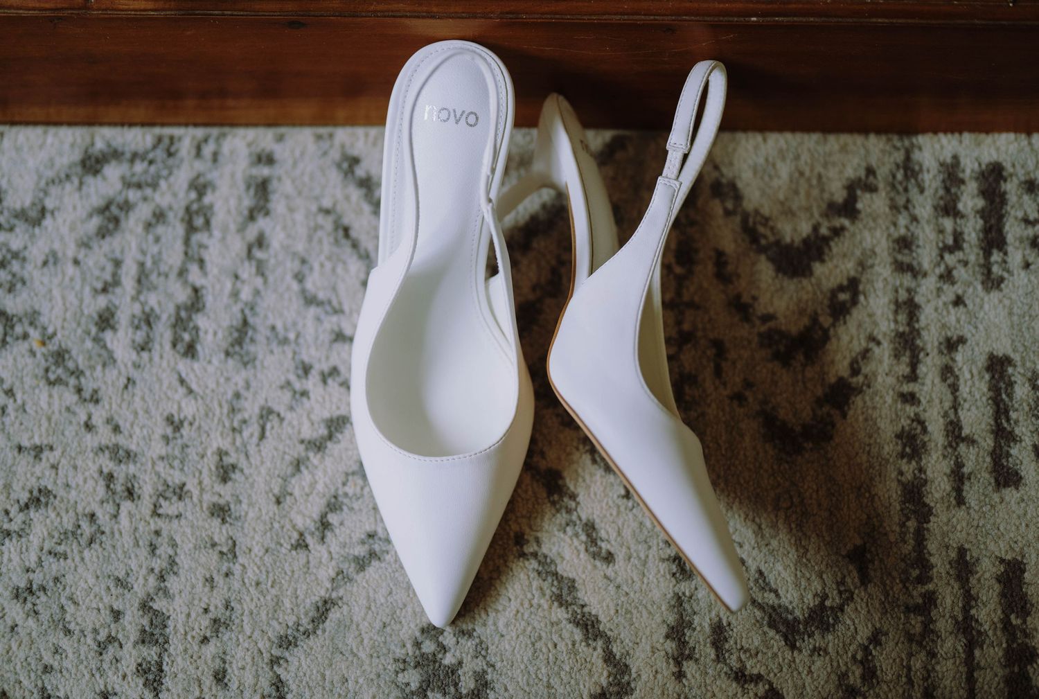 White slingback pointed-toe heels displayed on a patterned area rug, perfect bridal wedding shoes.