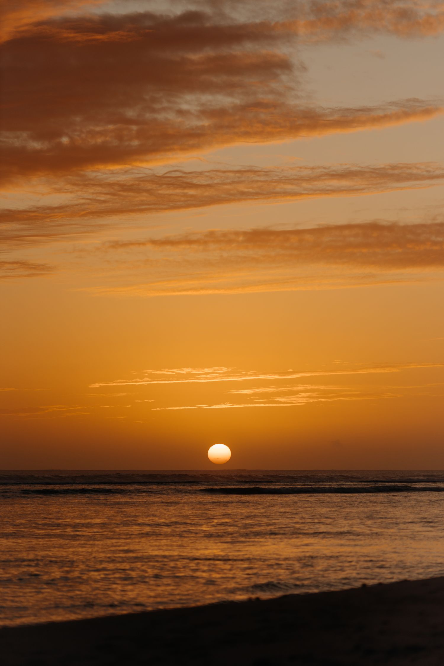 Golden sunset over calm ocean waves with dramatic orange sky and scattered clouds on the horizon.