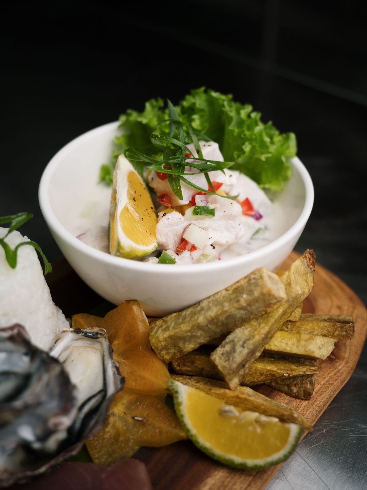 Fresh seafood ceviche bowl with shrimp, lemon, lettuce, oyster, and fried yuca on a wooden board.