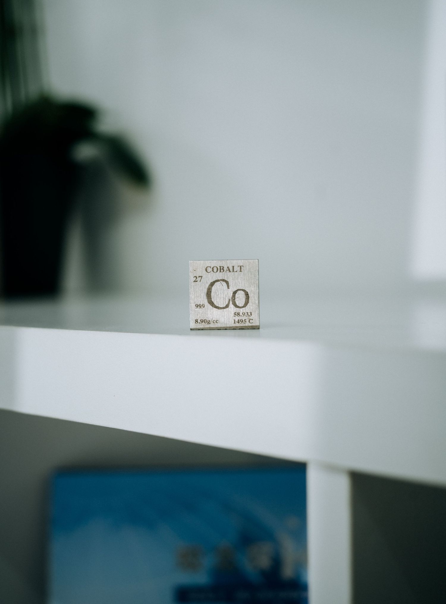 Cobalt element tile from the periodic table displayed on a white shelf in a modern minimalist room.