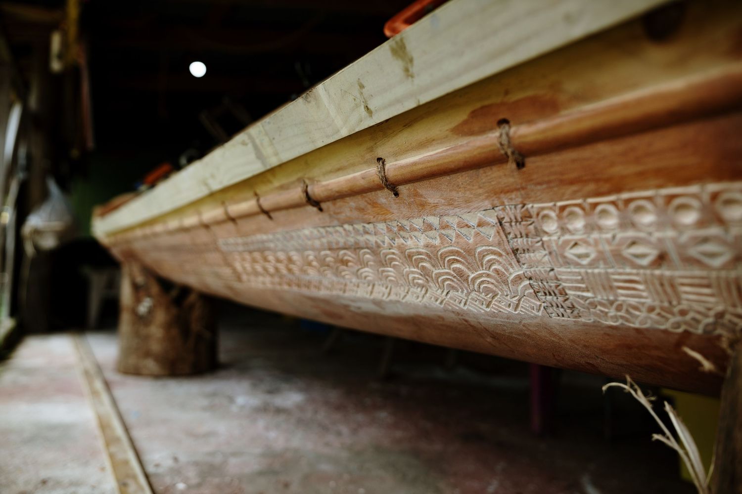 Intricately carved wooden canoe hull with traditional Polynesian patterns displayed in a workshop.