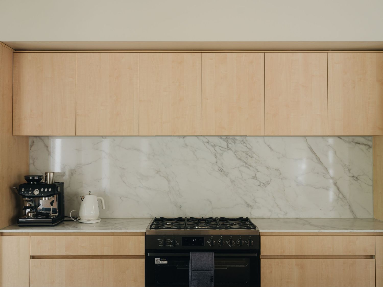 Modern kitchen with light wood cabinets, marble backsplash, and black gas range stove.