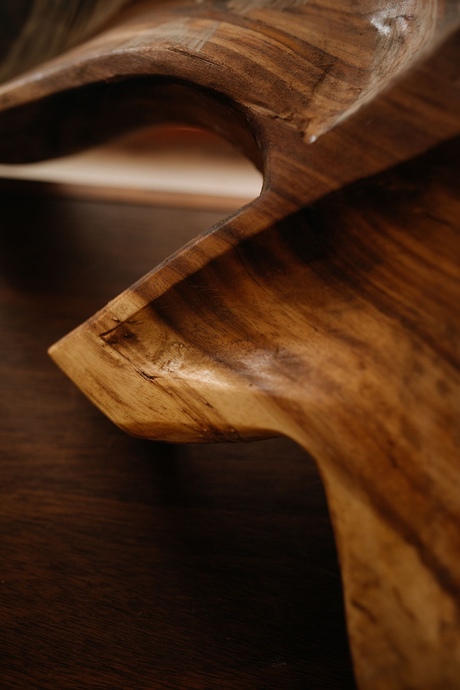 Close-up of a polished wooden sculpture with smooth curves and rich grain detail on a dark wood surface.