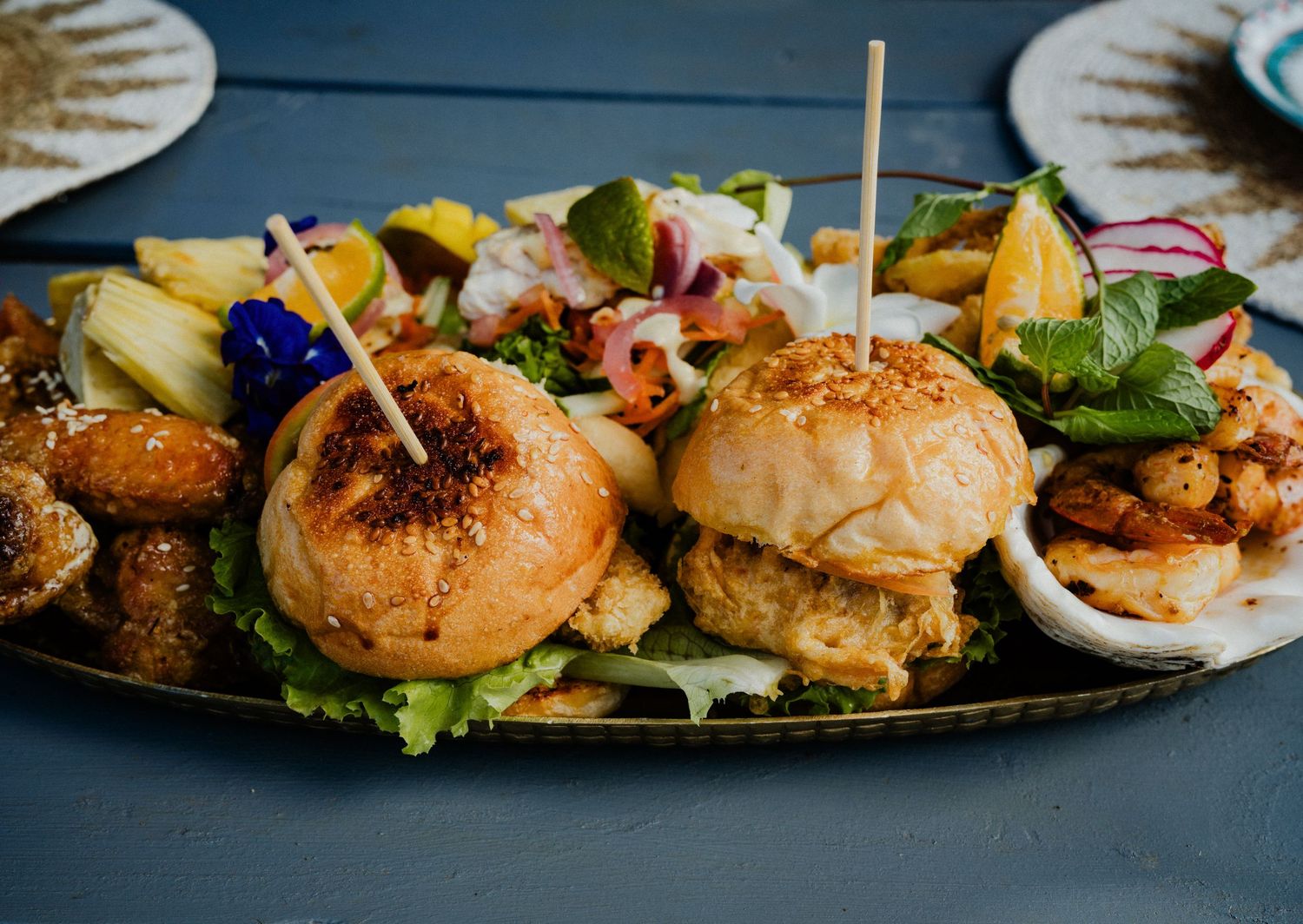 A platter of mini sliders, shrimp, and fresh salad garnished with toothpick skewers on a rustic tray.