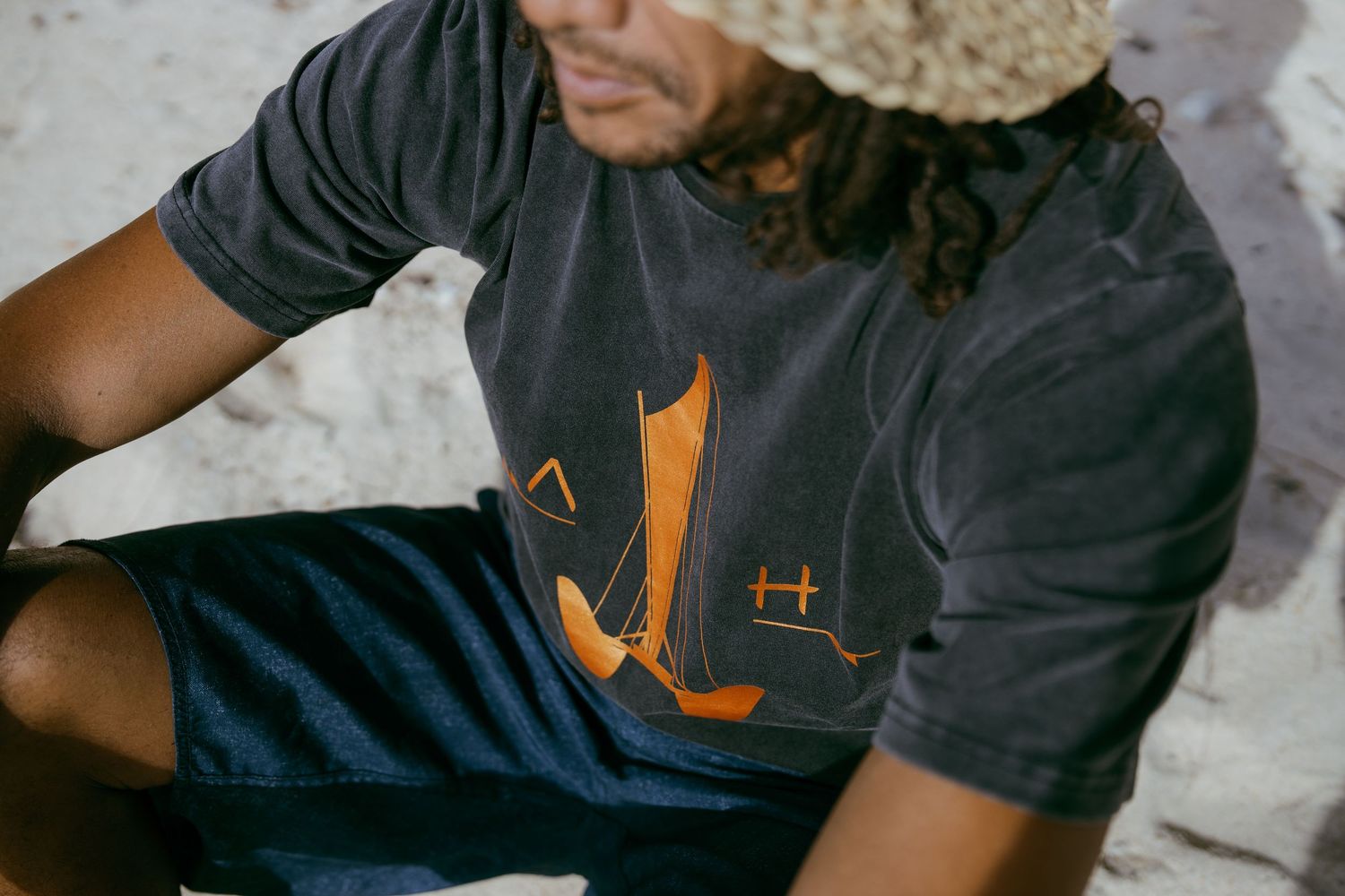 Person wearing a dark gray graphic t-shirt with orange print and blue shorts, sitting casually outdoors.
