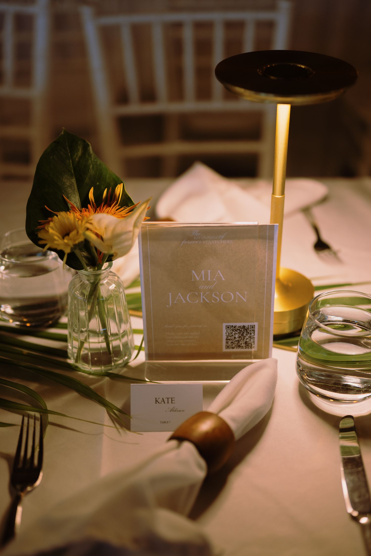 Elegant wedding table setting with gold lamp, floral centerpiece, place card reading Kate, and menu card for Mia & Jackson.