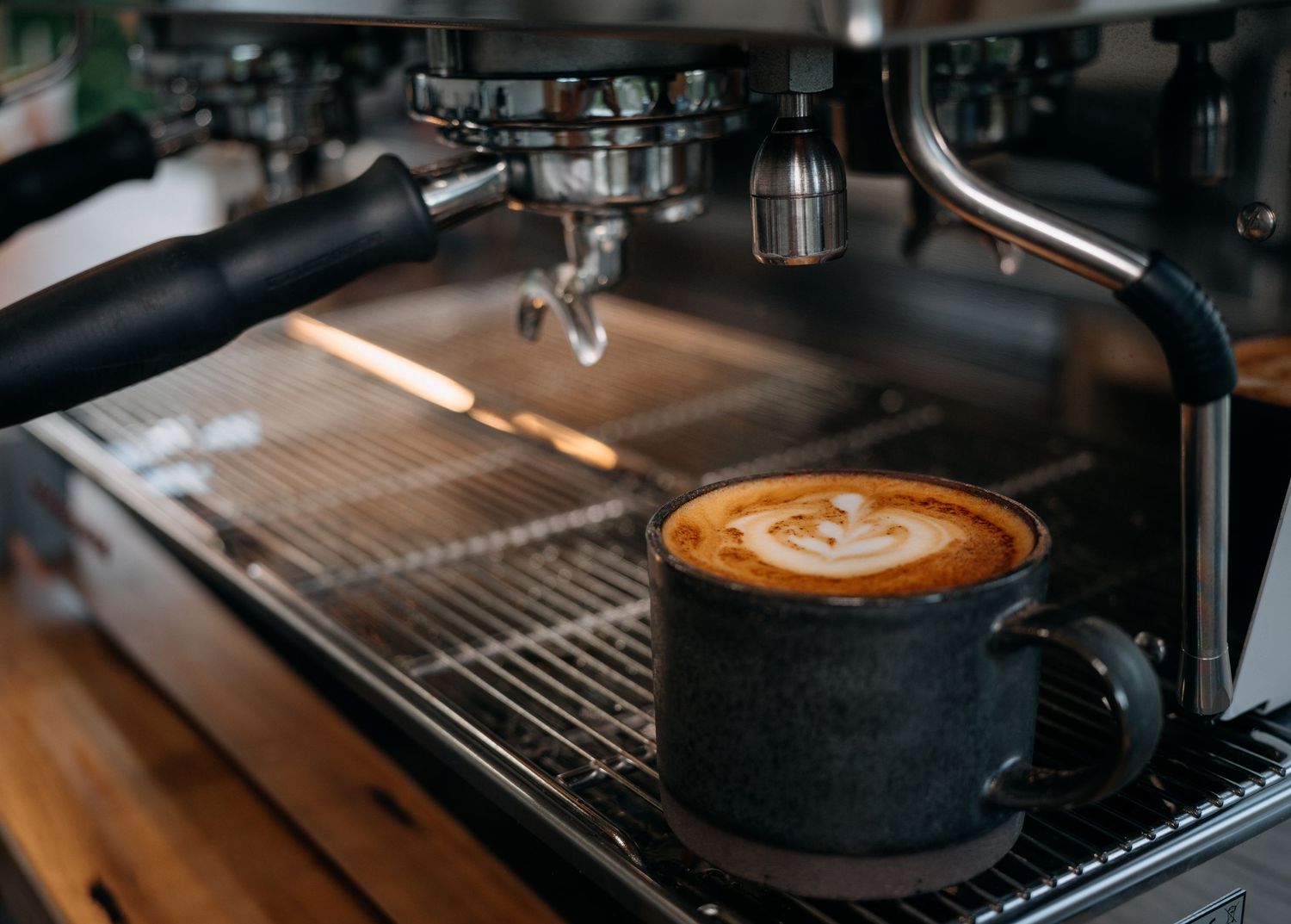 A freshly brewed latte with latte art sits in a dark mug on a professional espresso machine drip tray.