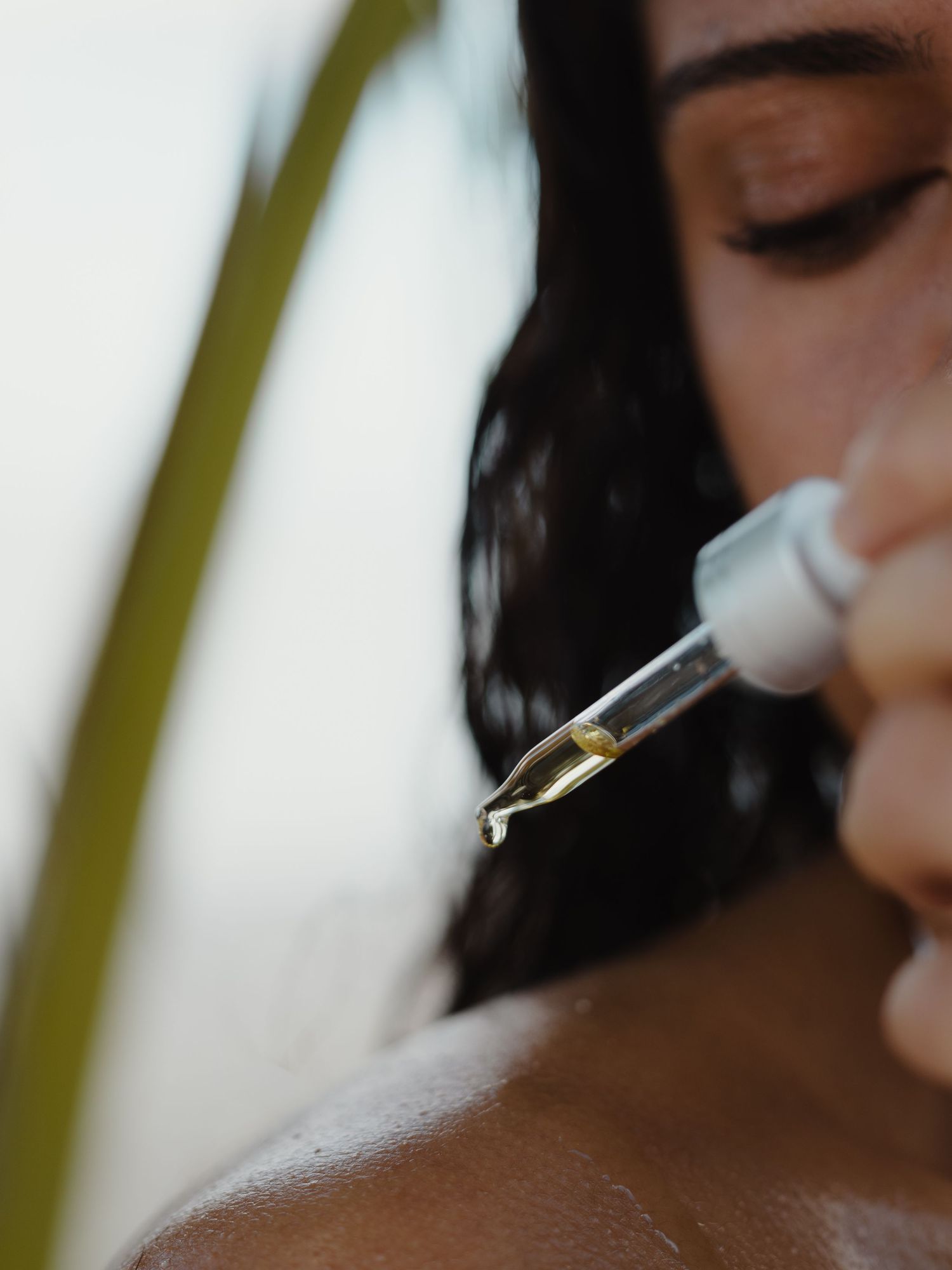 A woman applying golden facial oil serum with a dropper onto her glowing skin for a skincare routine.
