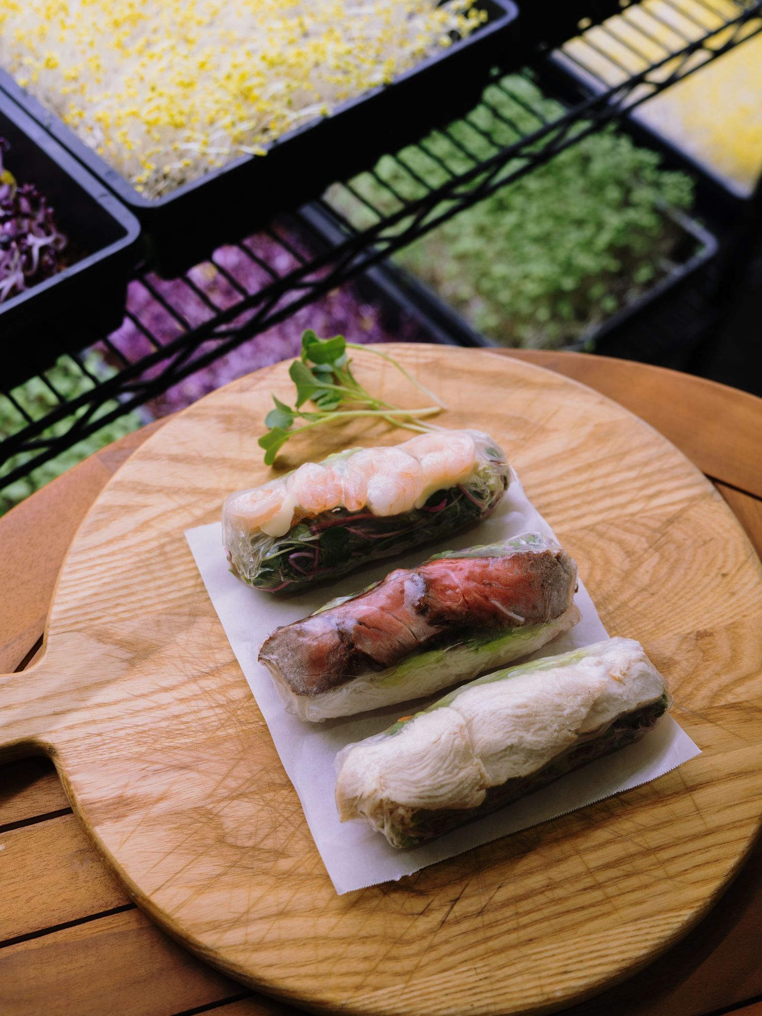 Fresh Vietnamese spring rolls with shrimp on a wooden board, with colorful ingredient trays in the background.