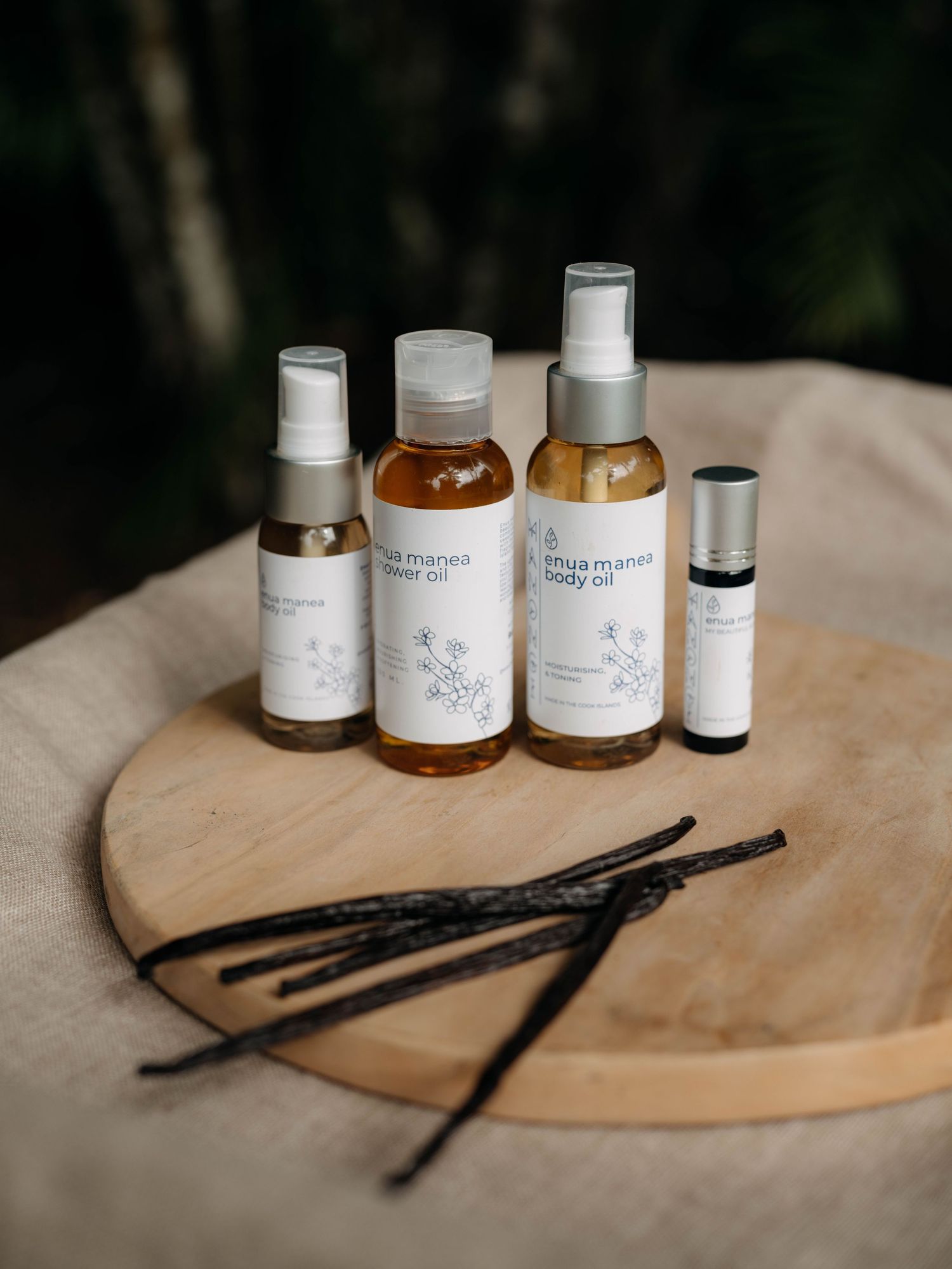 Natural body oils and roller bottle by Inya Manes displayed on wooden board with vanilla beans.