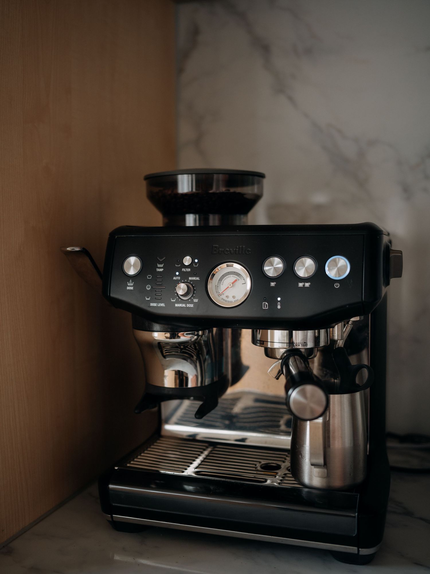 Black Breville espresso machine with built-in grinder and steam wand on marble countertop.