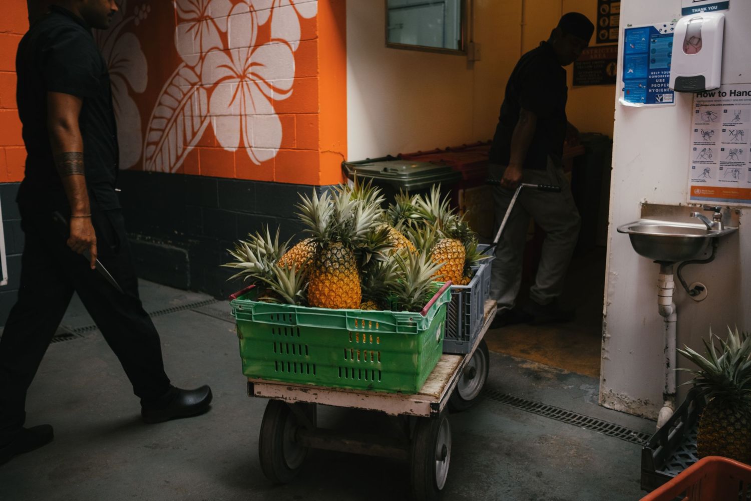 Fresh pineapples in a green crate on a cart being transported through a market corridor.