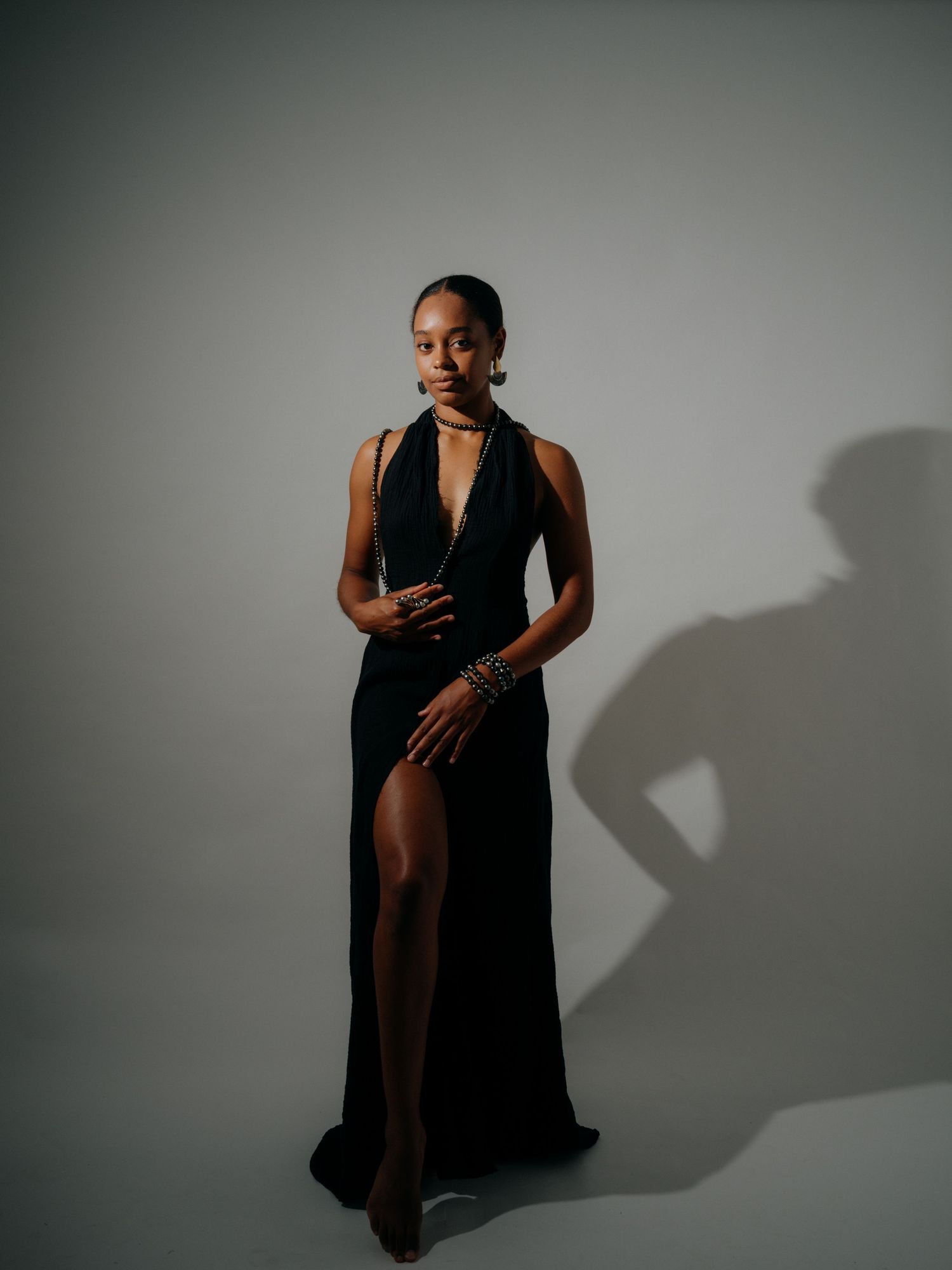Woman in elegant black halter gown with thigh slit poses gracefully against gray studio backdrop.