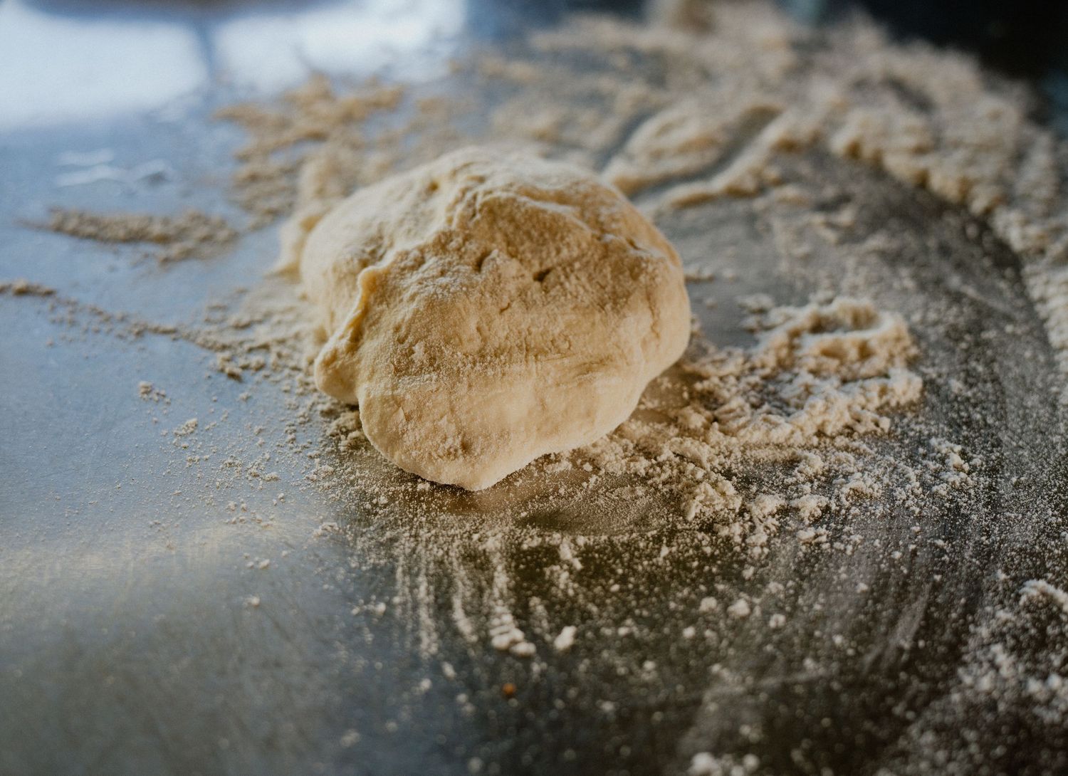 Close-up of a small dough ball dusted with flour on a lightly floured metal baking surface.