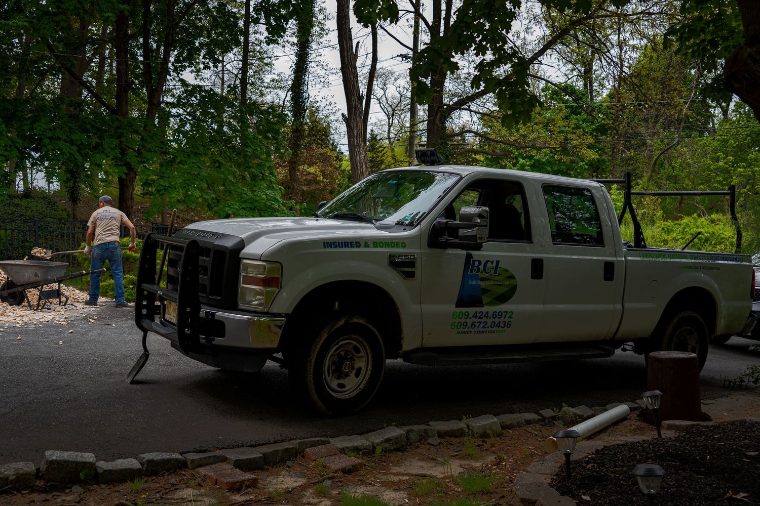 White work BCI truck parked on a driveway surrounded by trees on a cloudy day.