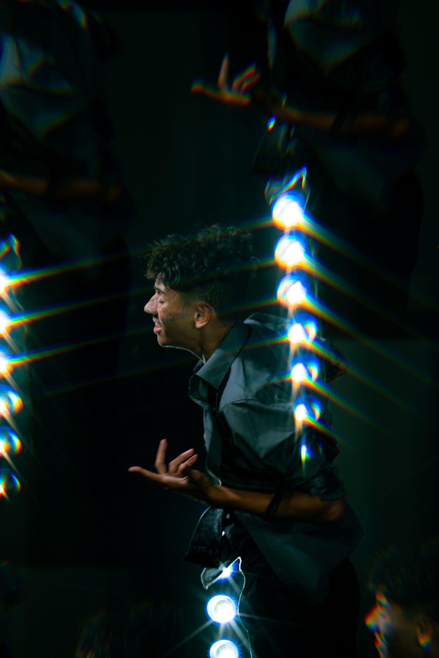 Young man performing on a dark stage surrounded by colorful lens flare light effects.