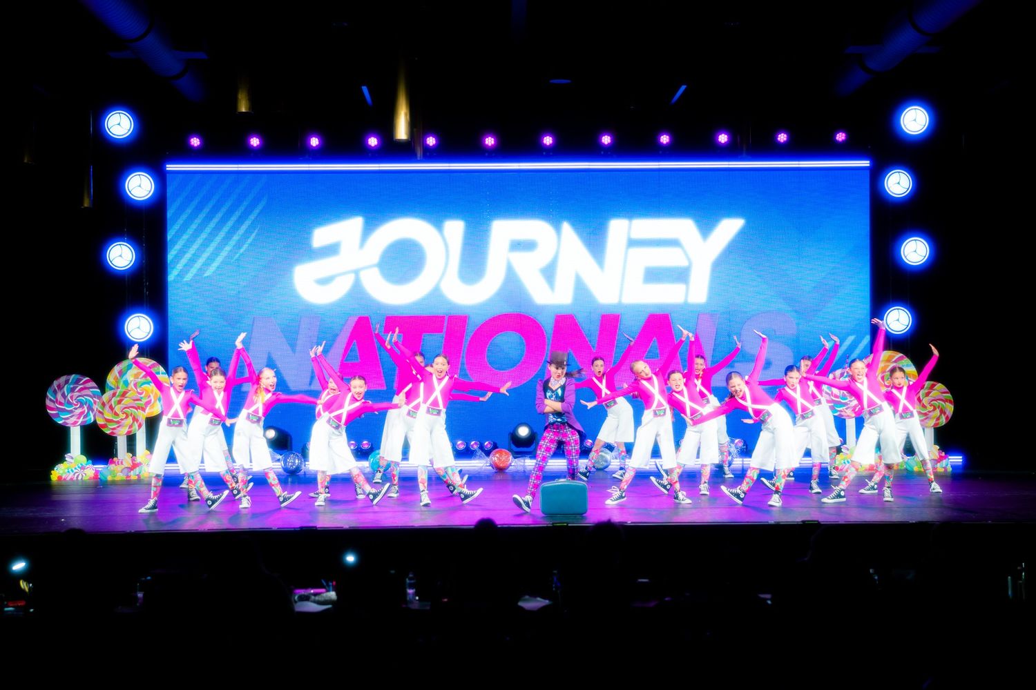 Colorful Journey Nationals dance performance on stage with large LED backdrop and dancers in white and pink costumes.