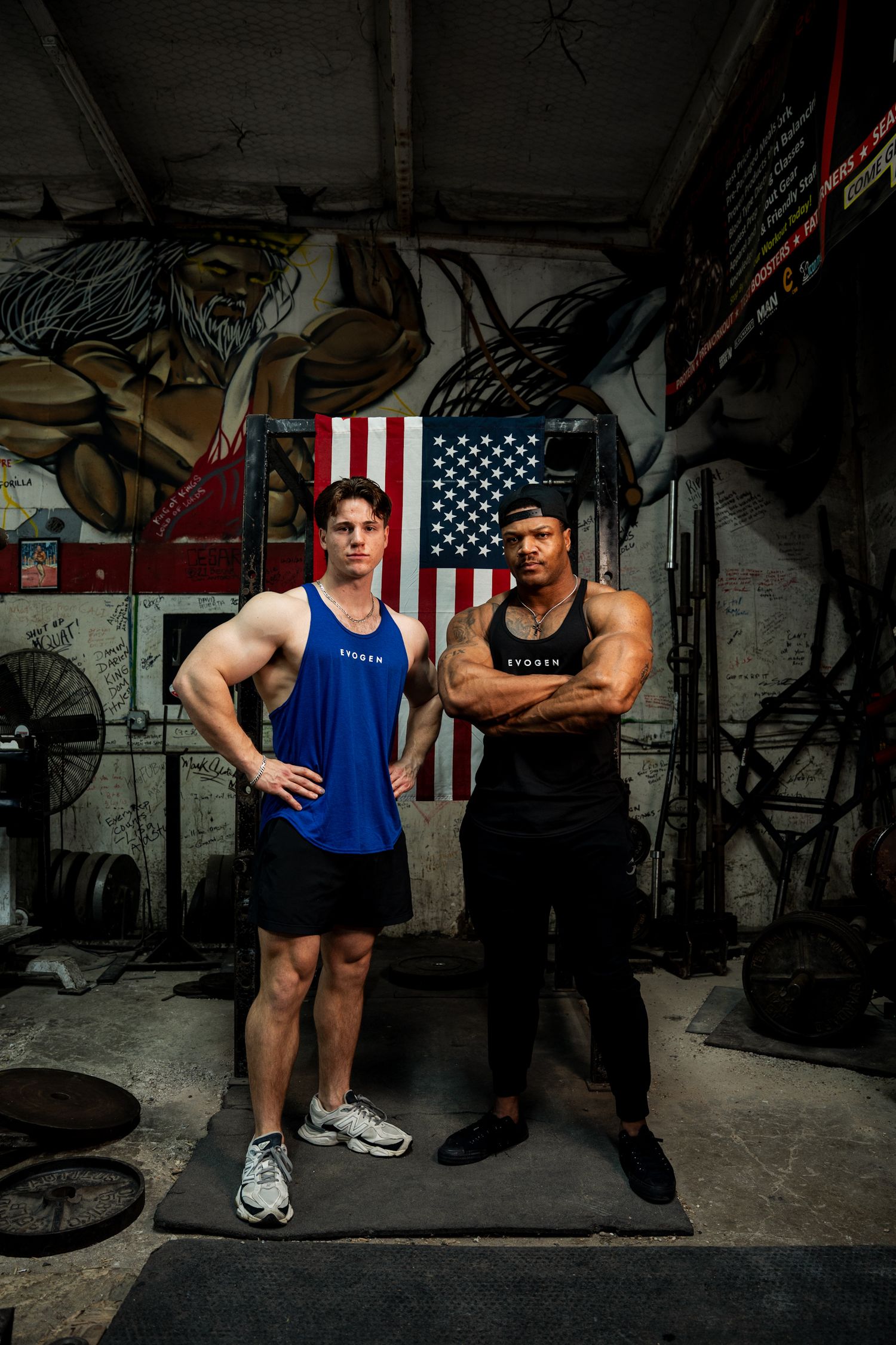 Two muscular men in Evogen athletic wear pose in a gym with an American flag backdrop.
