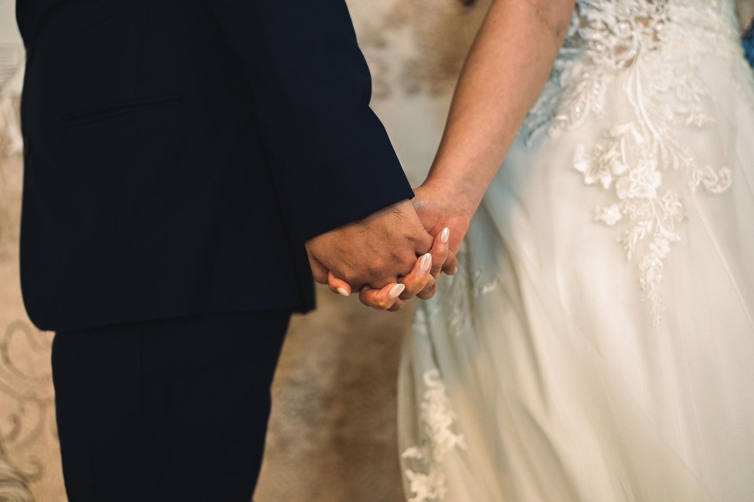 Close-up of bride and groom holding hands in wedding attire.