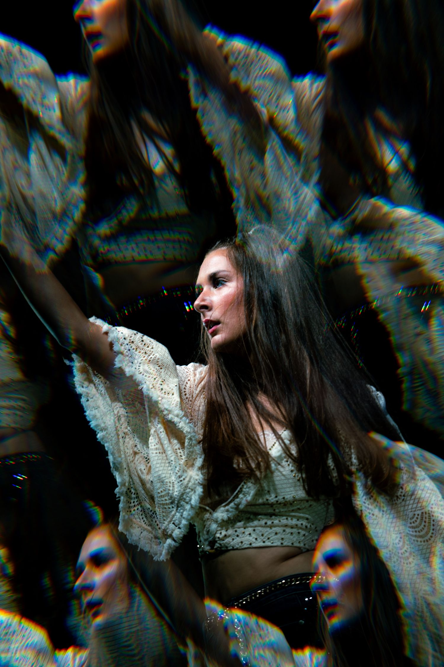 Woman in white lace outfit with multiple exposure effect creating ethereal, kaleidoscopic reflections against dark background.