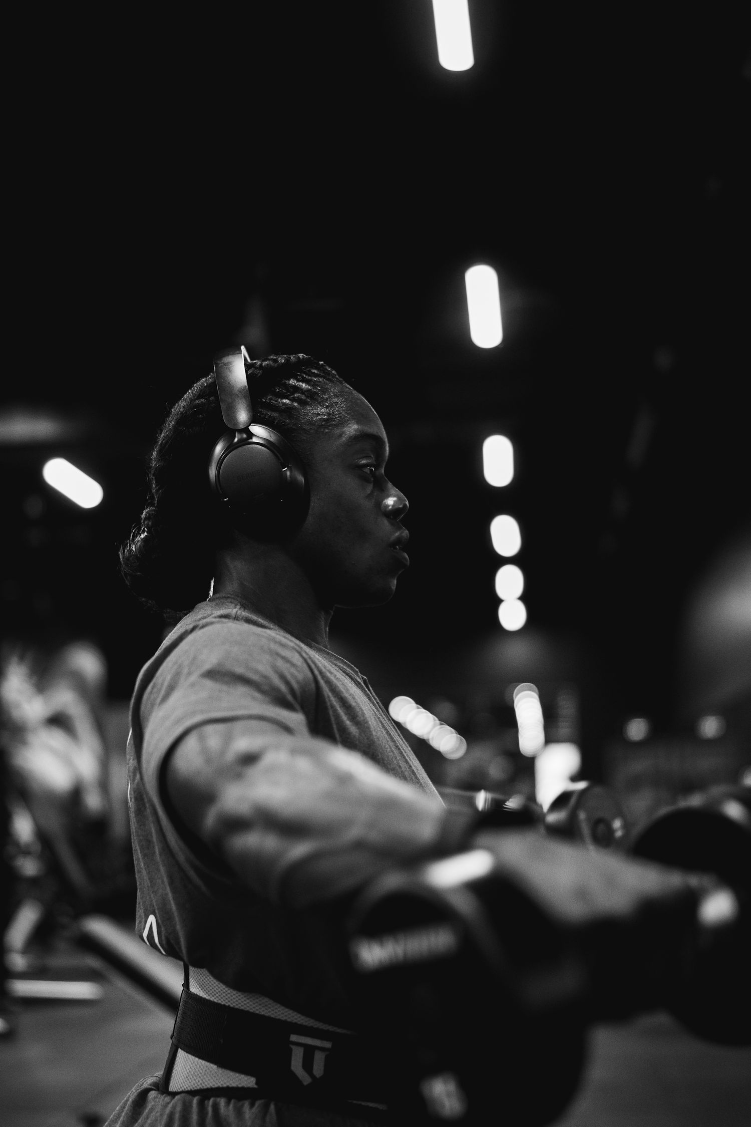 Black and white portrait of focused young Black athlete wearing headphones during gym workout.
