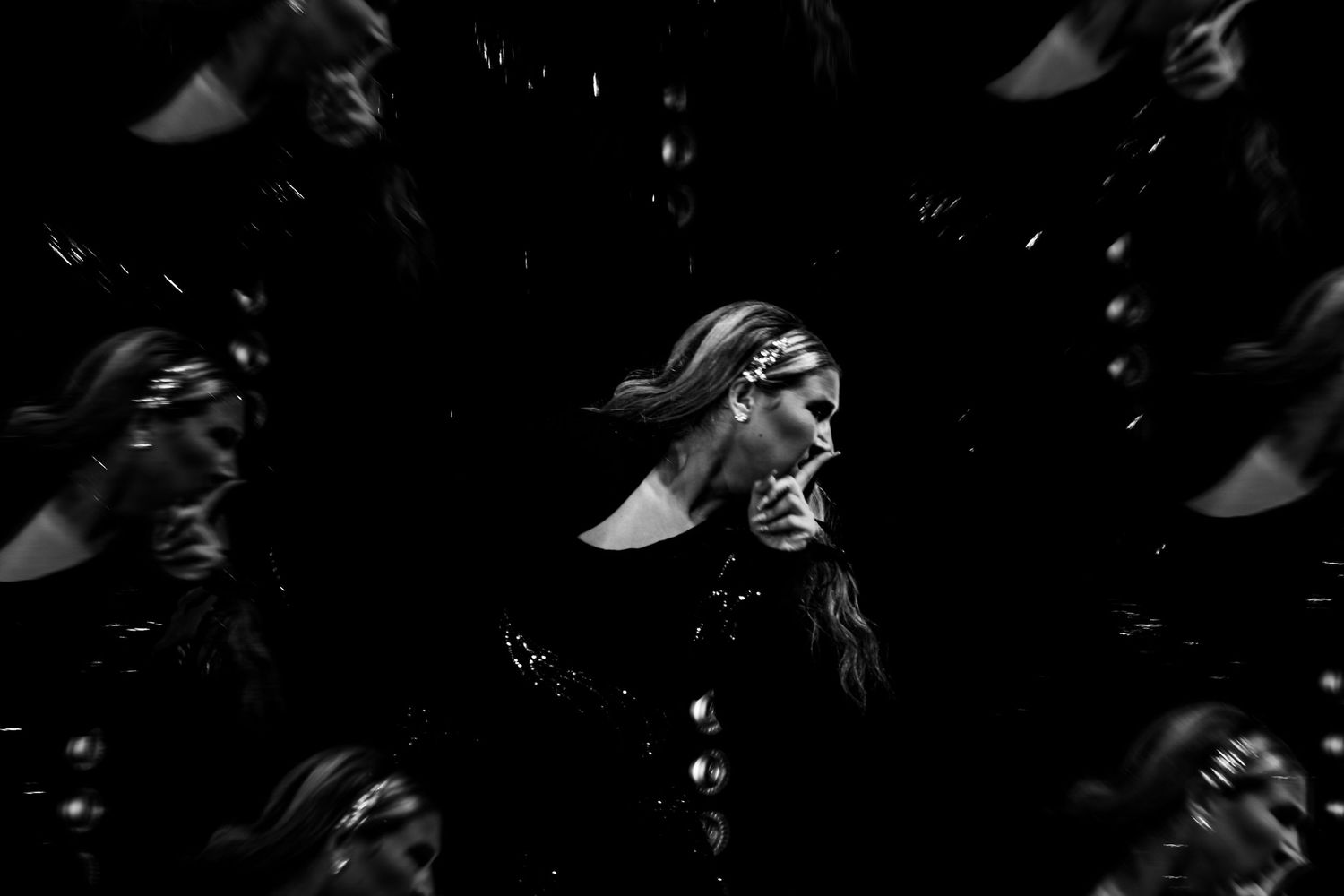 Black and white artistic photo of a woman surrounded by mirrored reflections in a dark, dramatic composition.