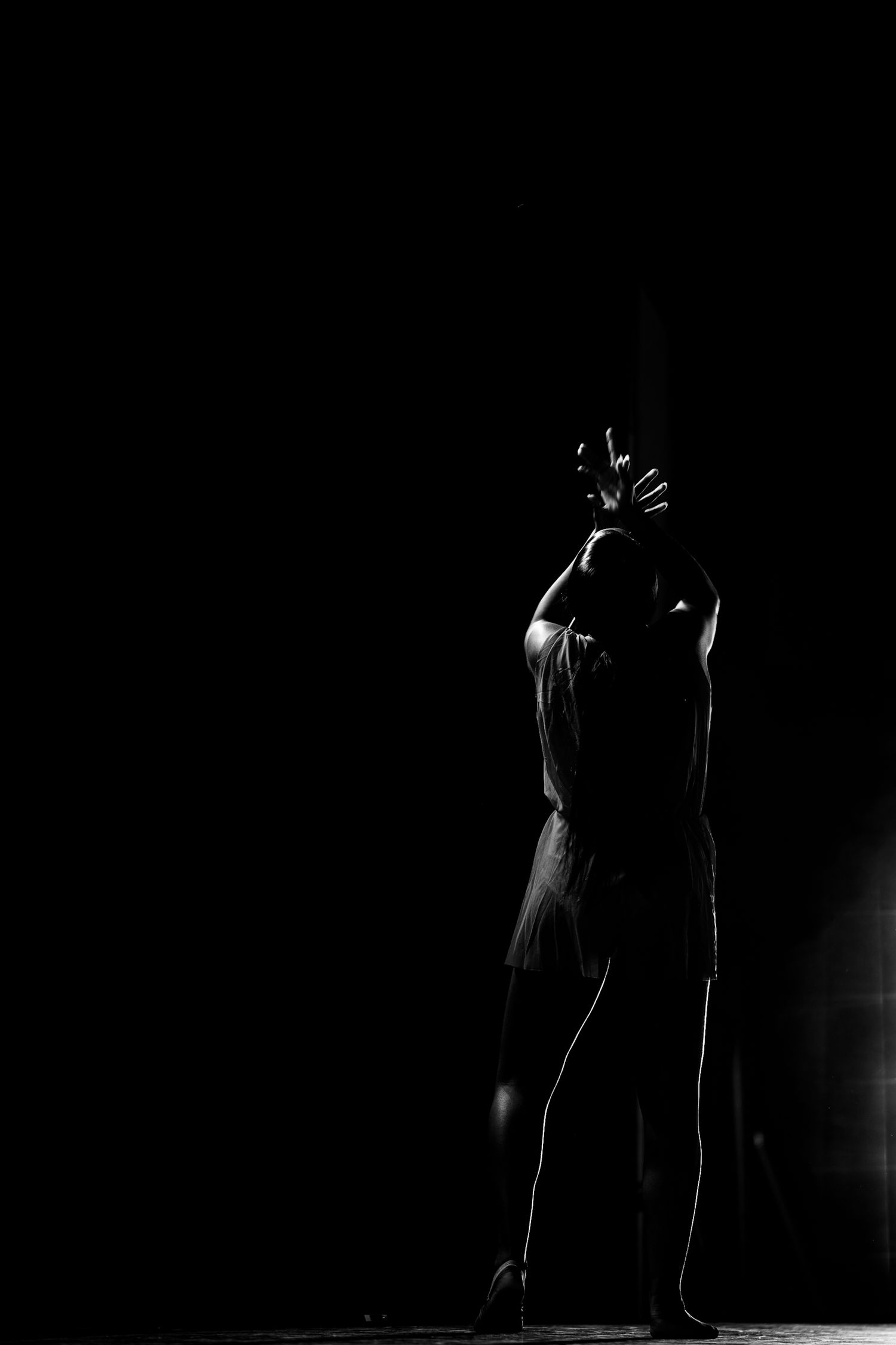Dramatic black and white silhouette of a dancer performing on stage with a single spotlight in the dark.