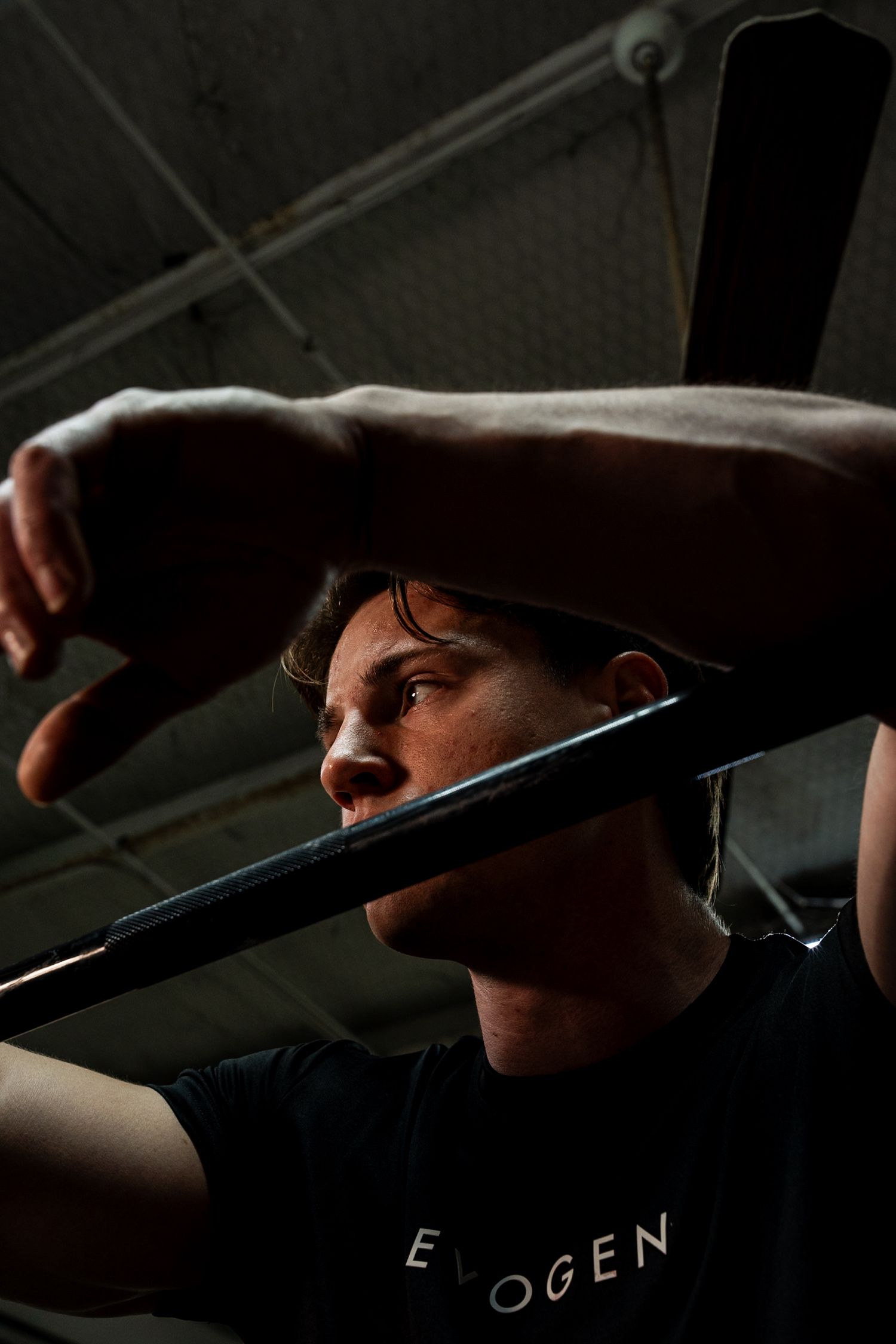 Athletic man in black Evogen shirt grips a barbell in dramatic gym lighting.