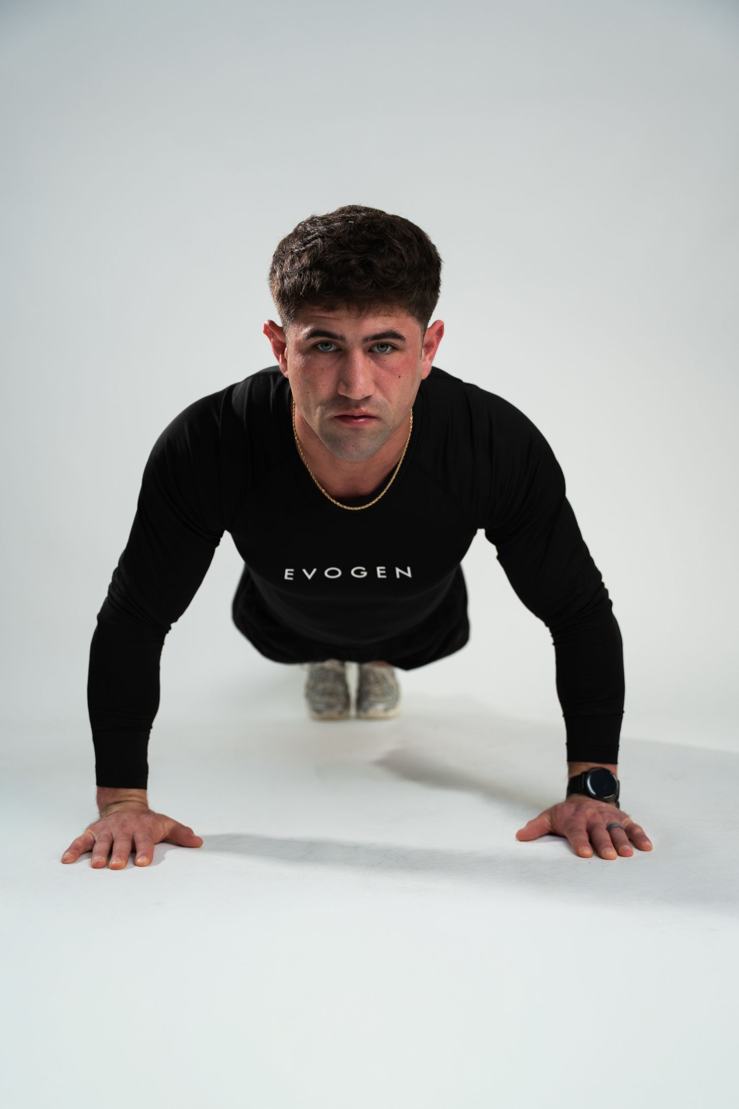 Fit man in black Evogen long-sleeve shirt performs a push-up on white studio background.