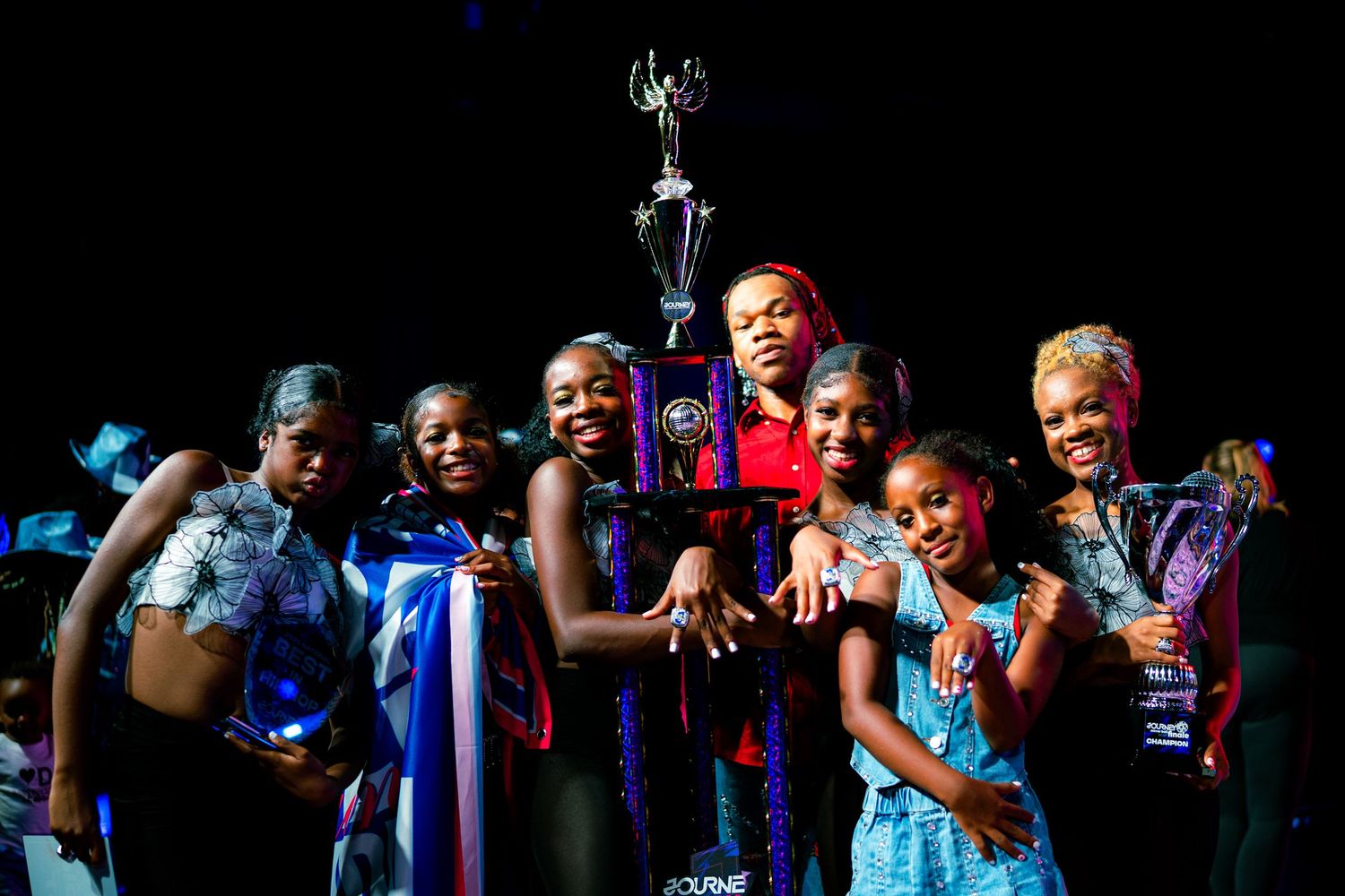 Group of young girls celebrating with a large trophy on stage after winning a dance competition.