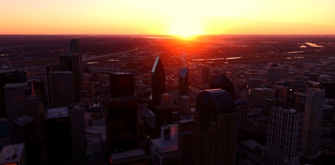 Stunning aerial sunset view over a major city skyline with glowing orange horizon and river.