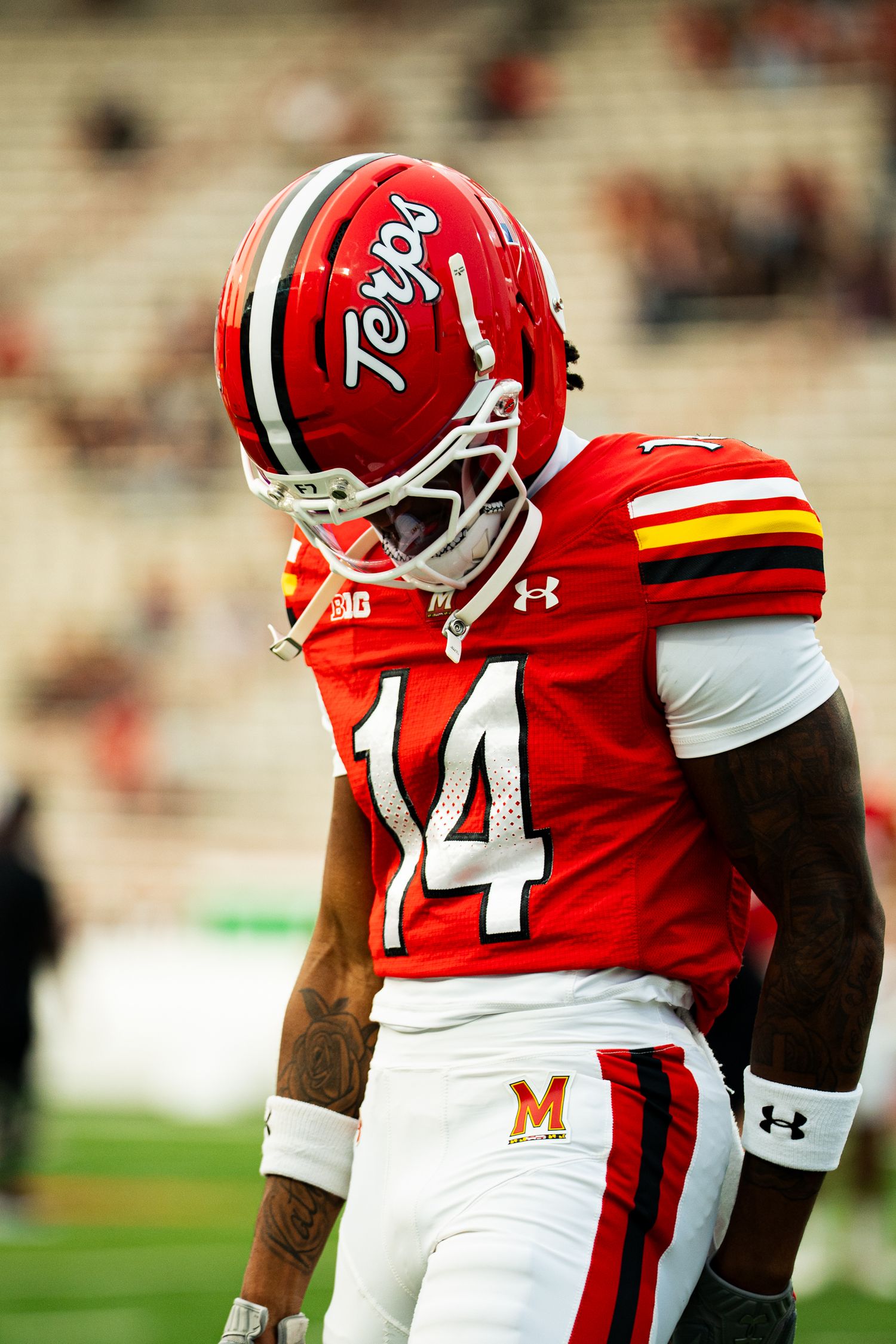 Maryland Terrapins football player #14 in red uniform and helmet on stadium field.