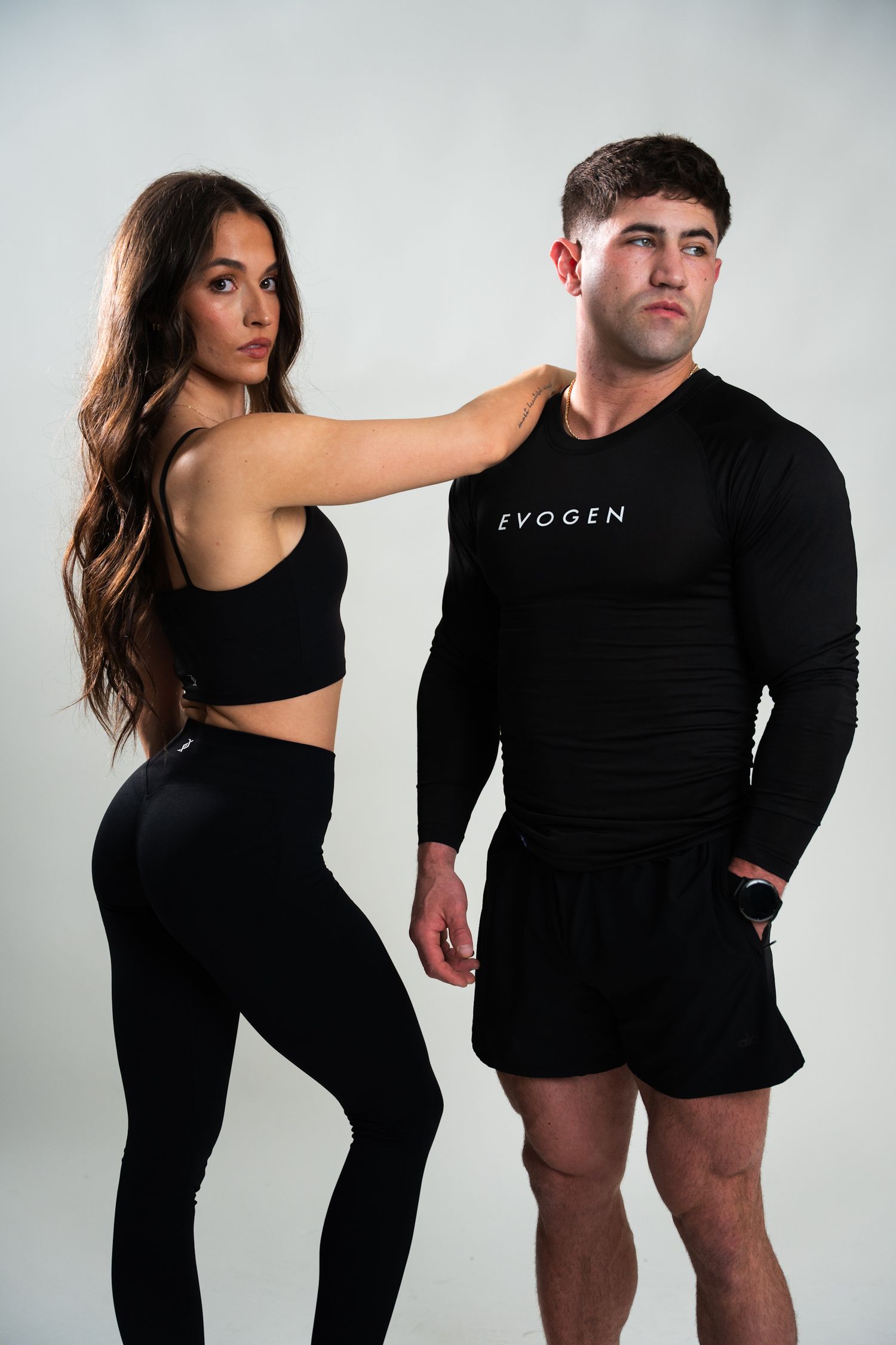 Fit couple posing in black Evogen athletic wear against white background in studio setting.
