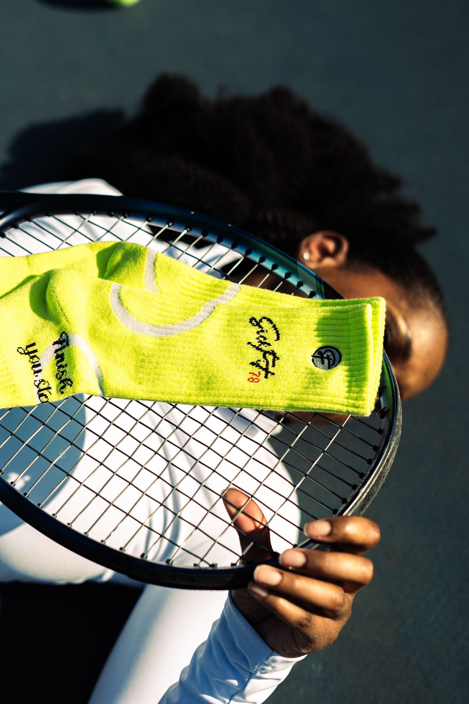 Tennis player holds racket with neon yellow headband, showcasing Graffiti and Prince branding on court.