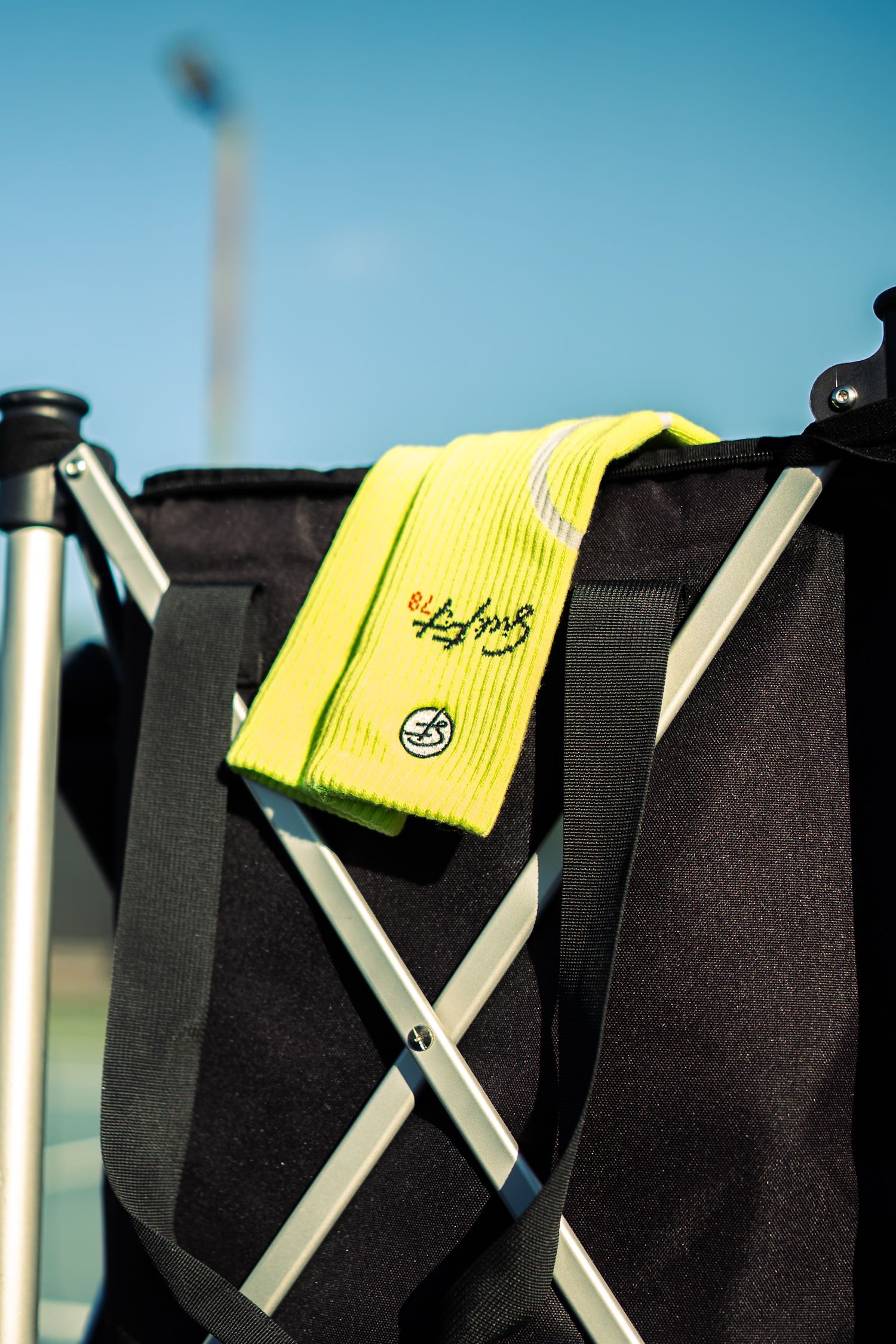 Neon yellow beanie with logo resting on a black bag with X-frame support against a blue sky.