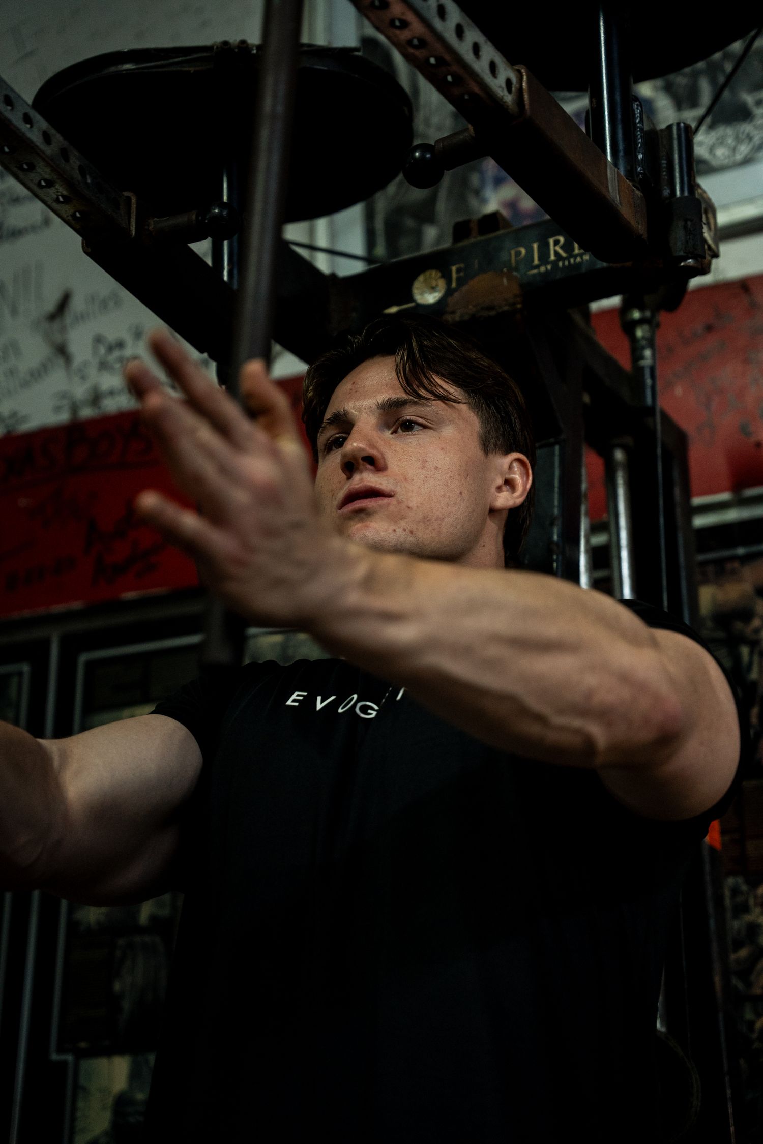 Young athletic man in black Evogen shirt reaching toward camera during intense gym workout session.