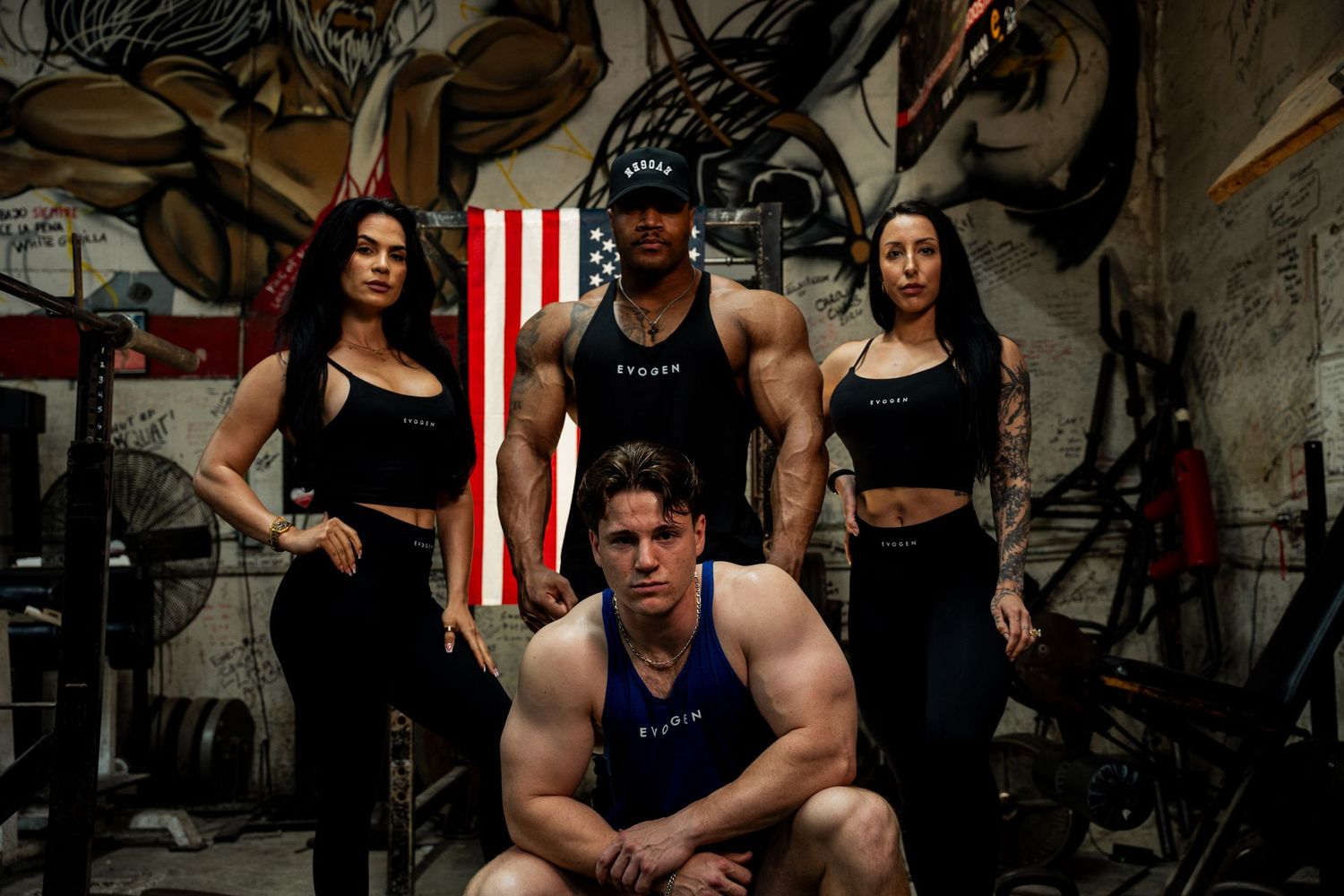 Four Evogen athletes pose together in a gritty gym with an American flag on the wall.