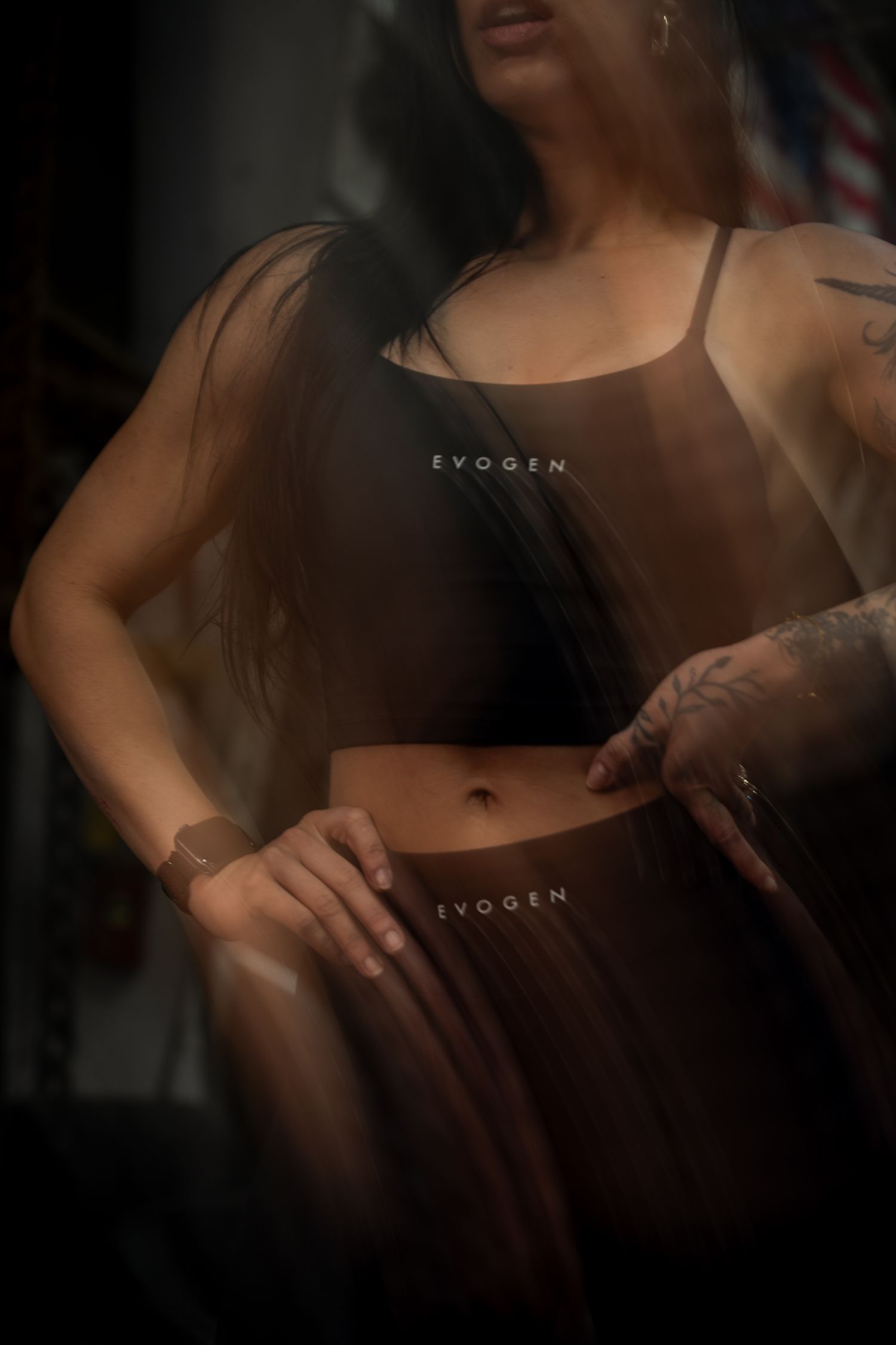 Woman wearing sheer Evogen branded crop top and skirt in dark studio.