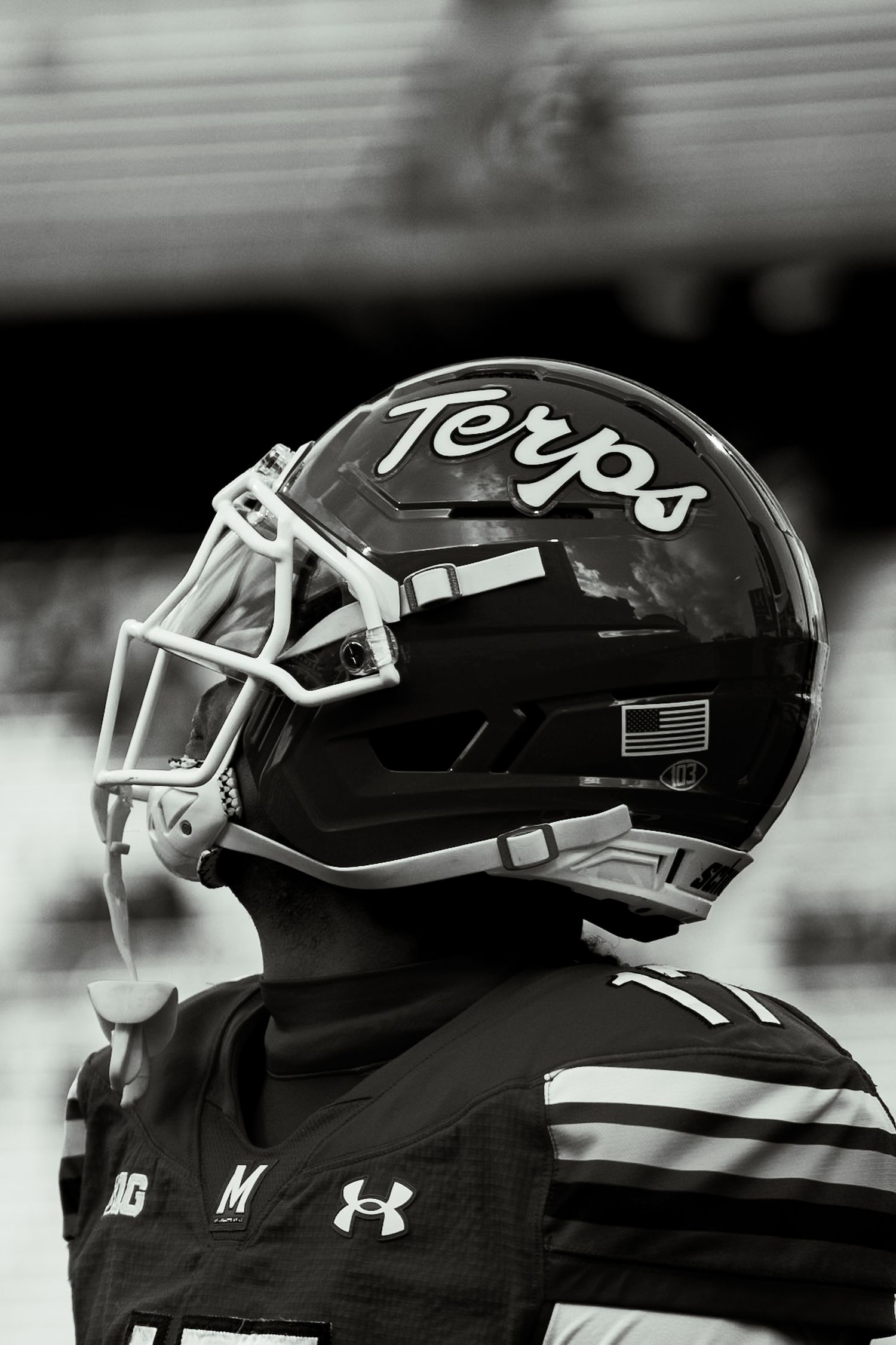 Black and white close-up profile shot of a Maryland Terrapins football player wearing a Terps helmet.