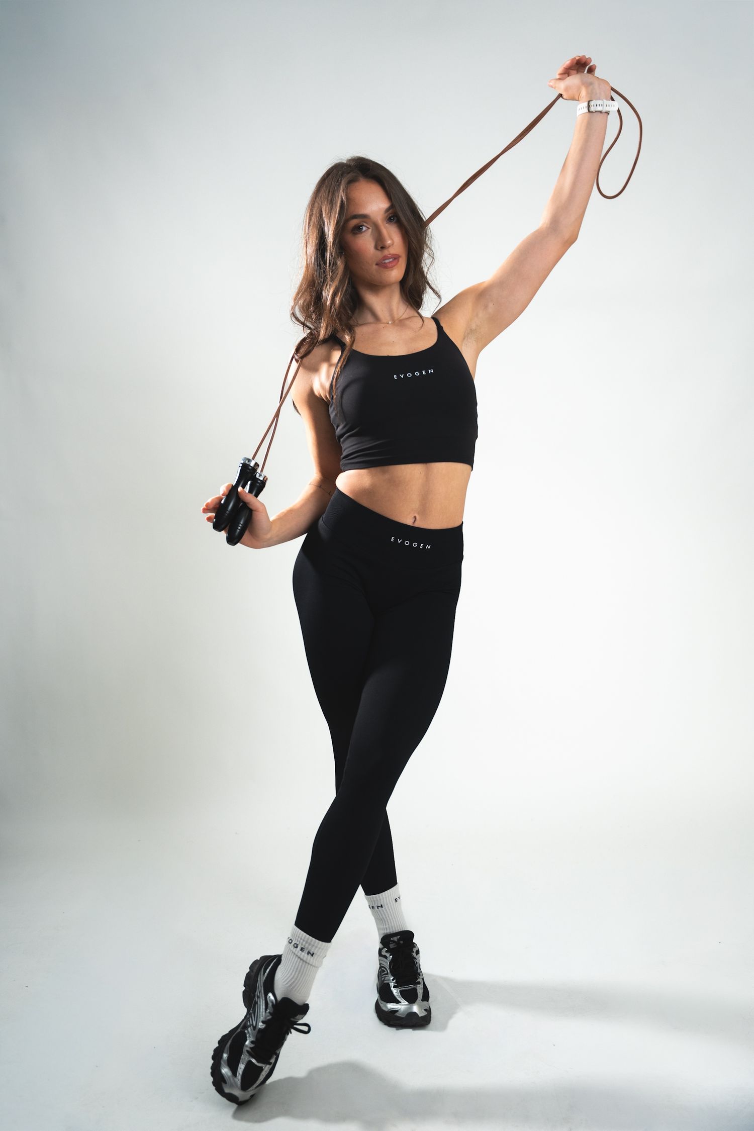 Fit woman in black Evogen activewear poses with a jump rope in a white studio setting.