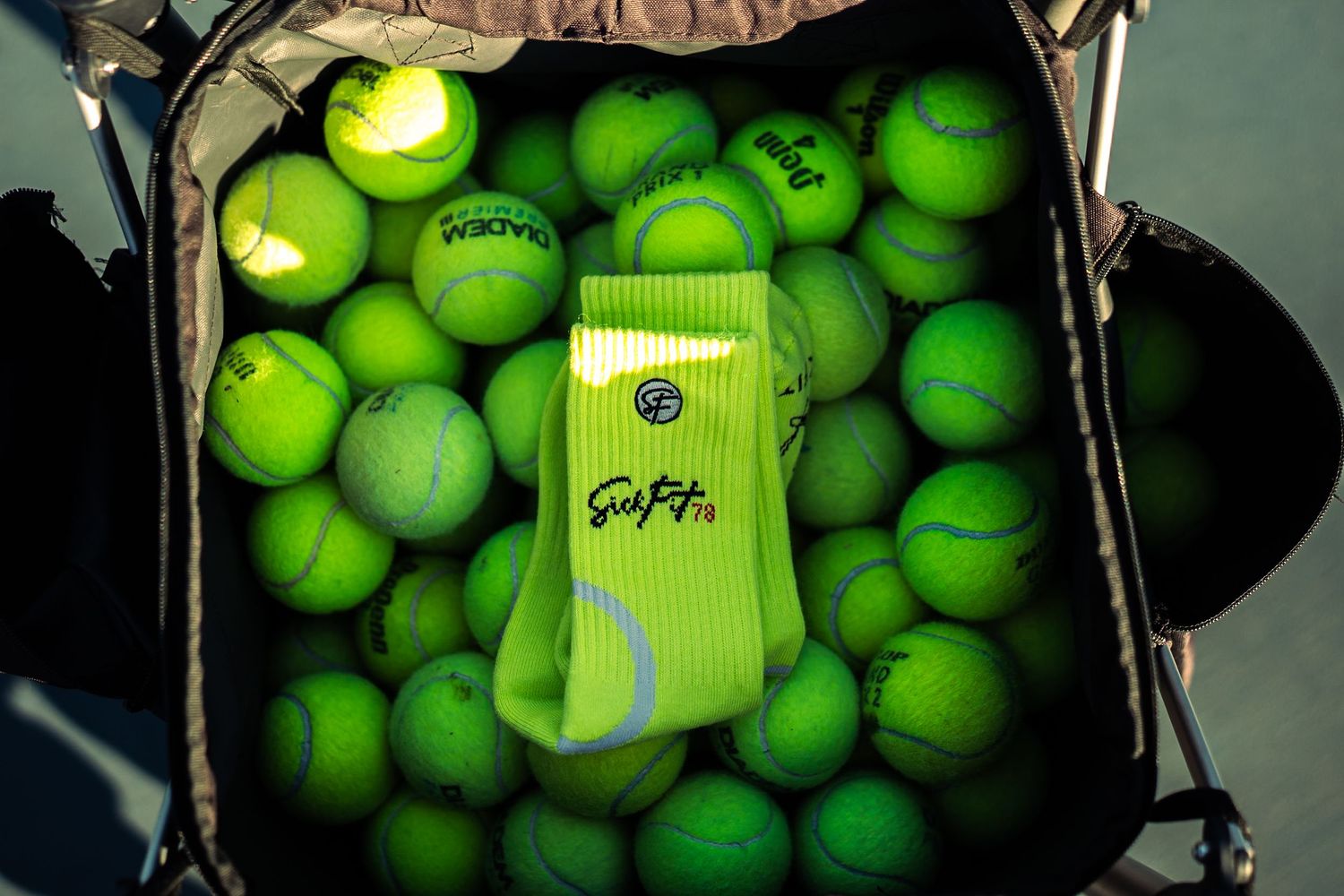 Bright green tennis socks with logo resting among a basket full of neon yellow Wimbledon tennis balls.