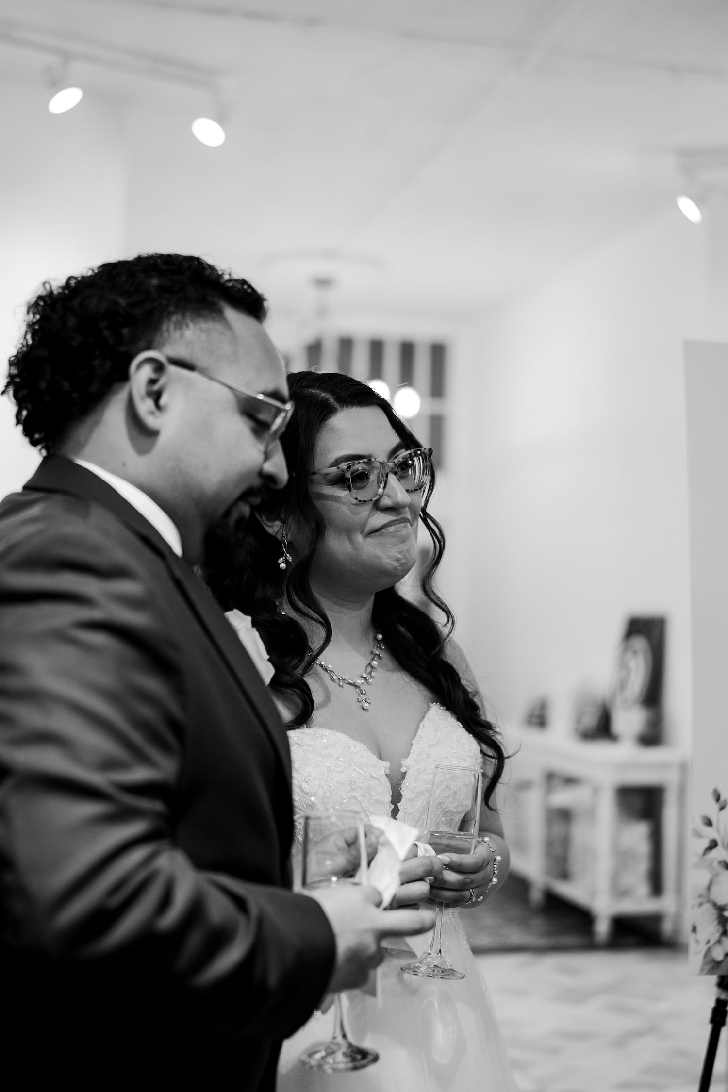 Black and white photo of bride and groom with glasses sharing a candid moment at reception.