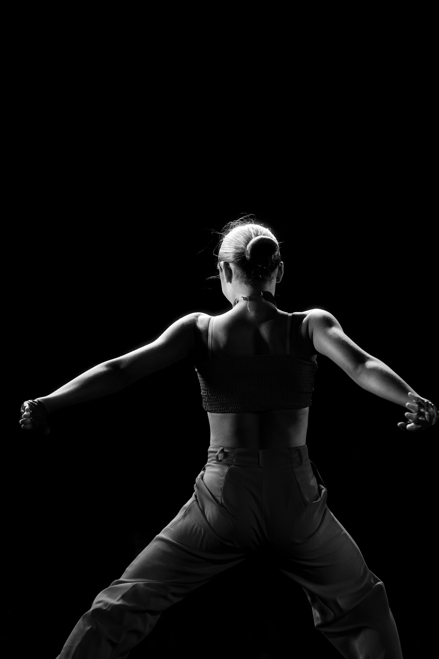 Black and white photo of a woman in athletic wear posing with arms outstretched against a dark background.