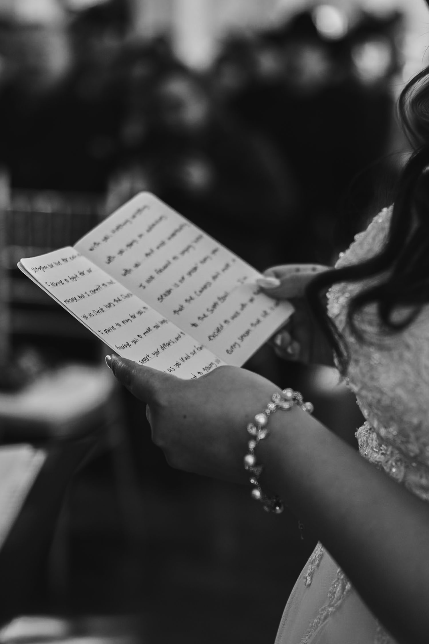 Black and white close-up of bride reading handwritten wedding vows wearing a pearl bracelet.