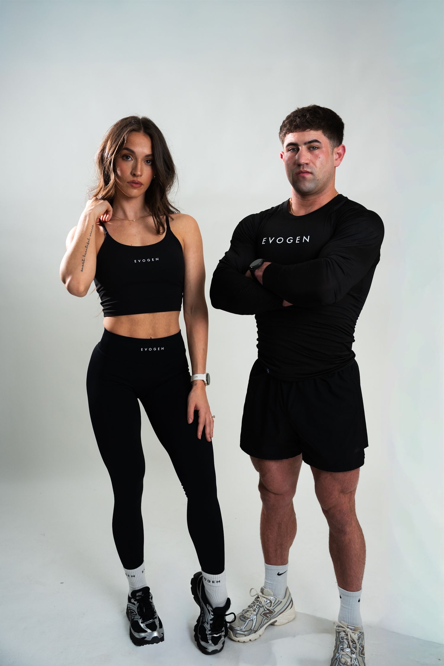 A fit man and woman in matching black Evogen athletic wear pose against a white background.