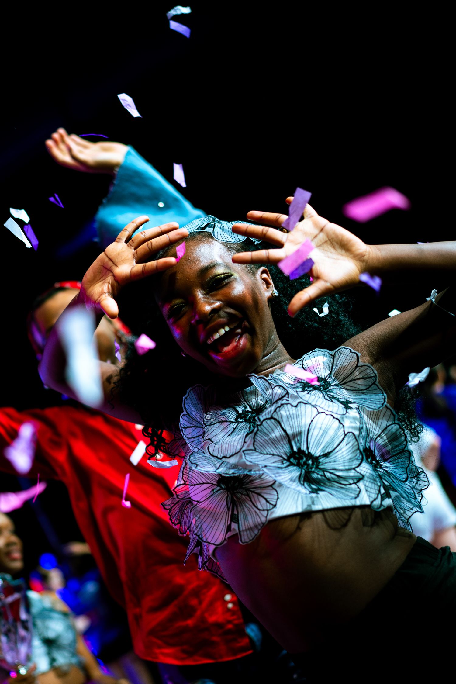 A joyful woman dances as colorful confetti falls around her at a vibrant celebration event.