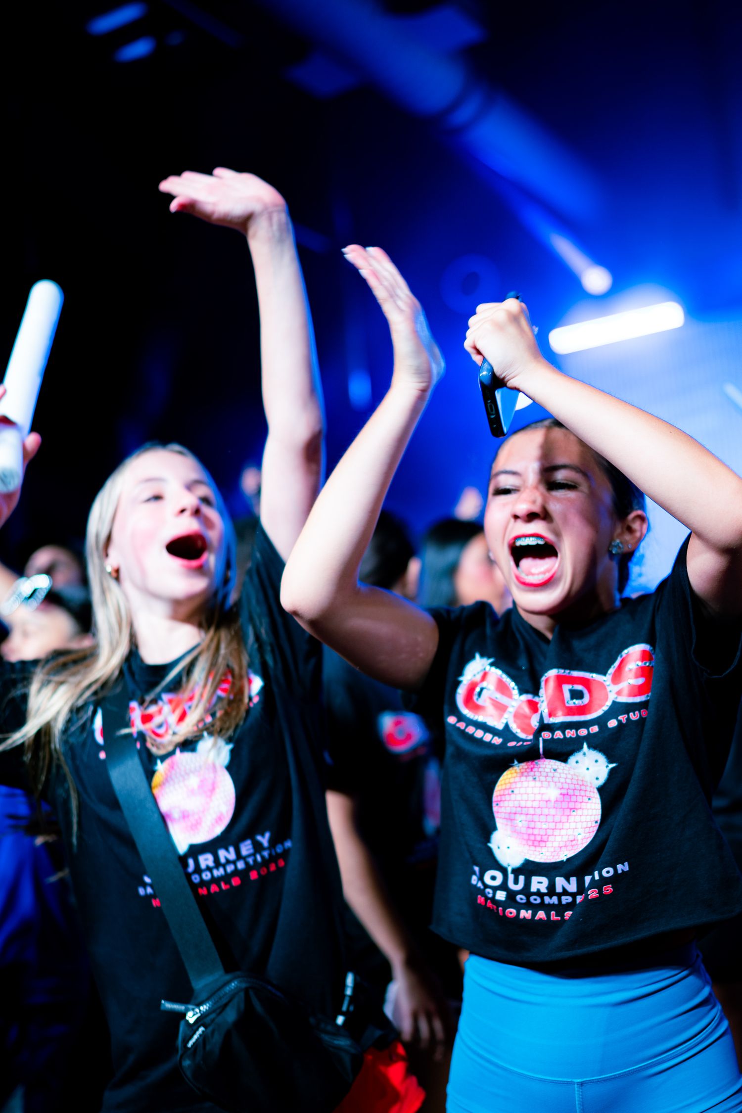 Excited young dancers in matching black GODS competition shirts cheering at a dance nationals event.