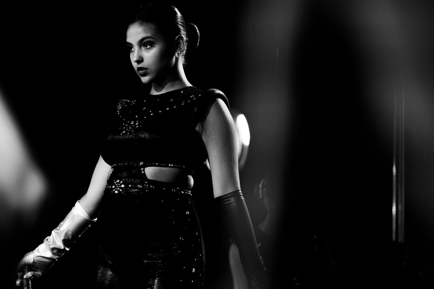 Black and white photo of a female dancer in a sparkly black outfit performing on a dimly lit stage.