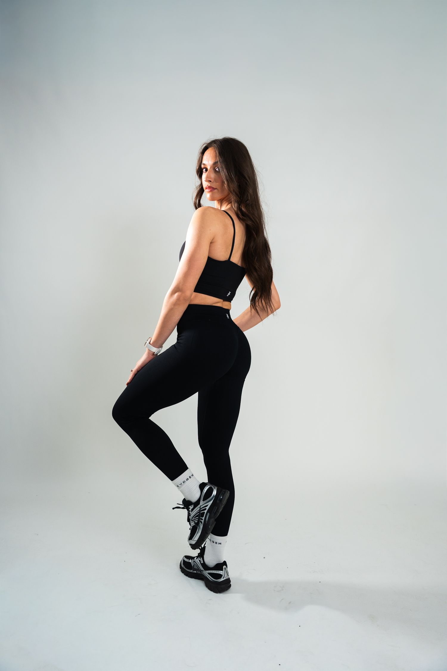 A fit woman in black Evogen sports bra and leggings poses against a white studio background.